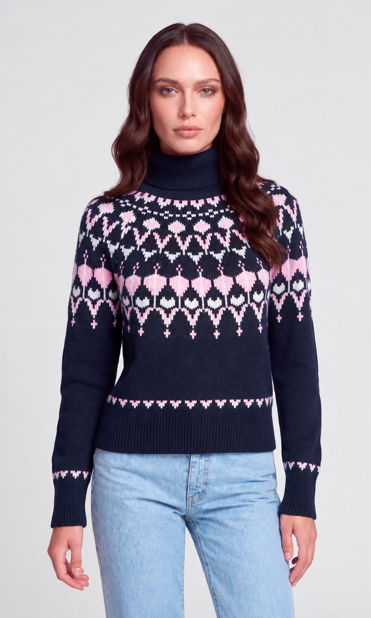 Model wearing a navy blue turtleneck sweater with a pink and white geometric Fair Isle pattern across the chest and sleeves.