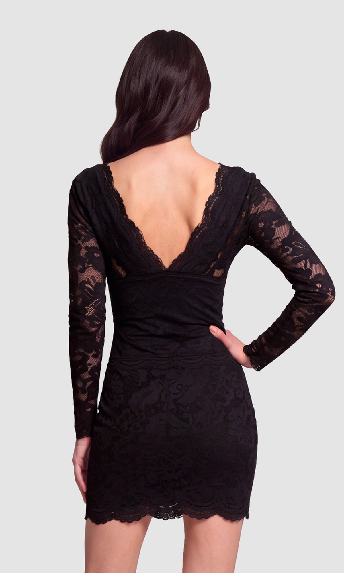 A woman shown from the back wearing a black lace long-sleeve mini dress with a deep V-neckline, set against a solid light gray background.
