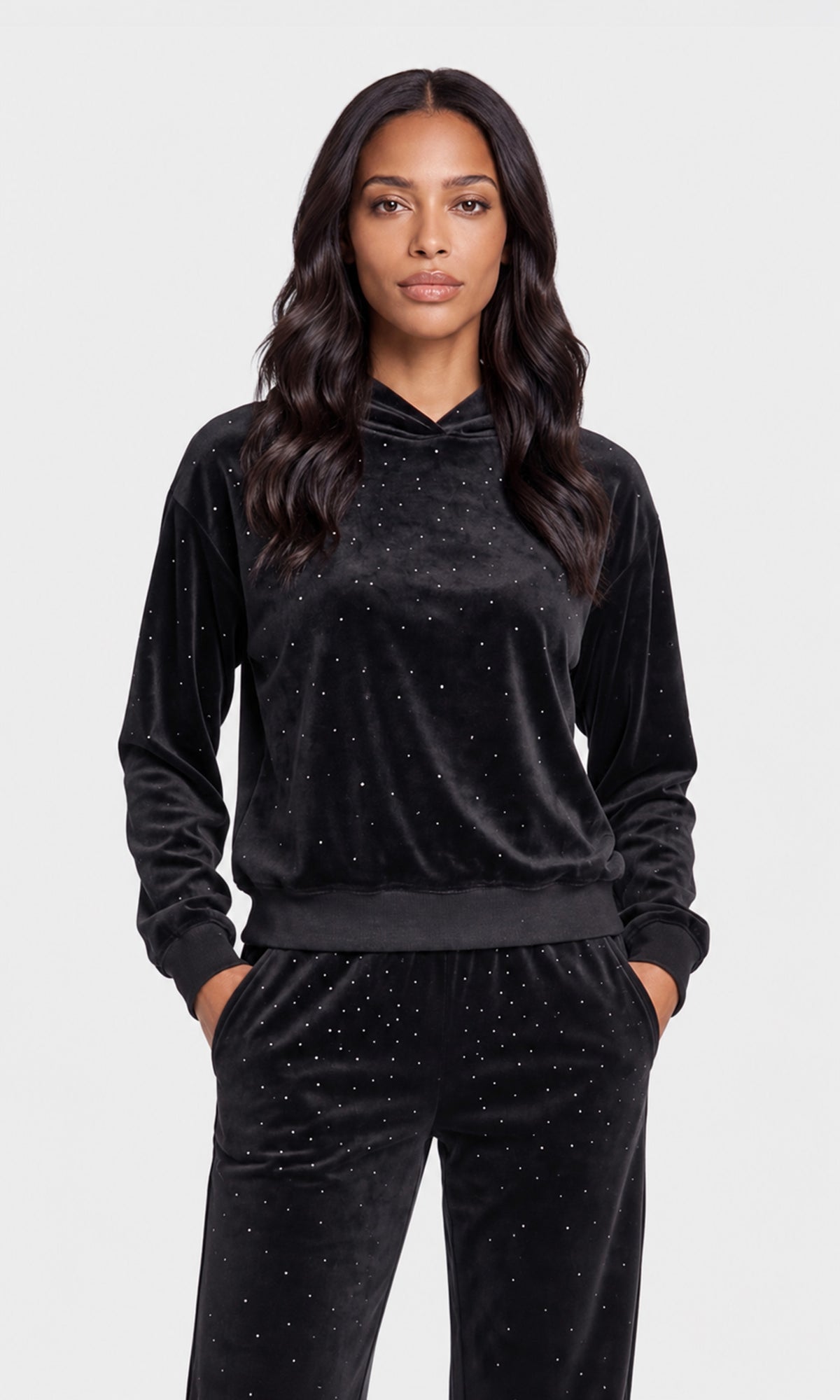Model wearing a black velvet two-piece loungewear set with subtle silver rhinestone embellishments, consisting of a long-sleeve hoodie and matching pants.