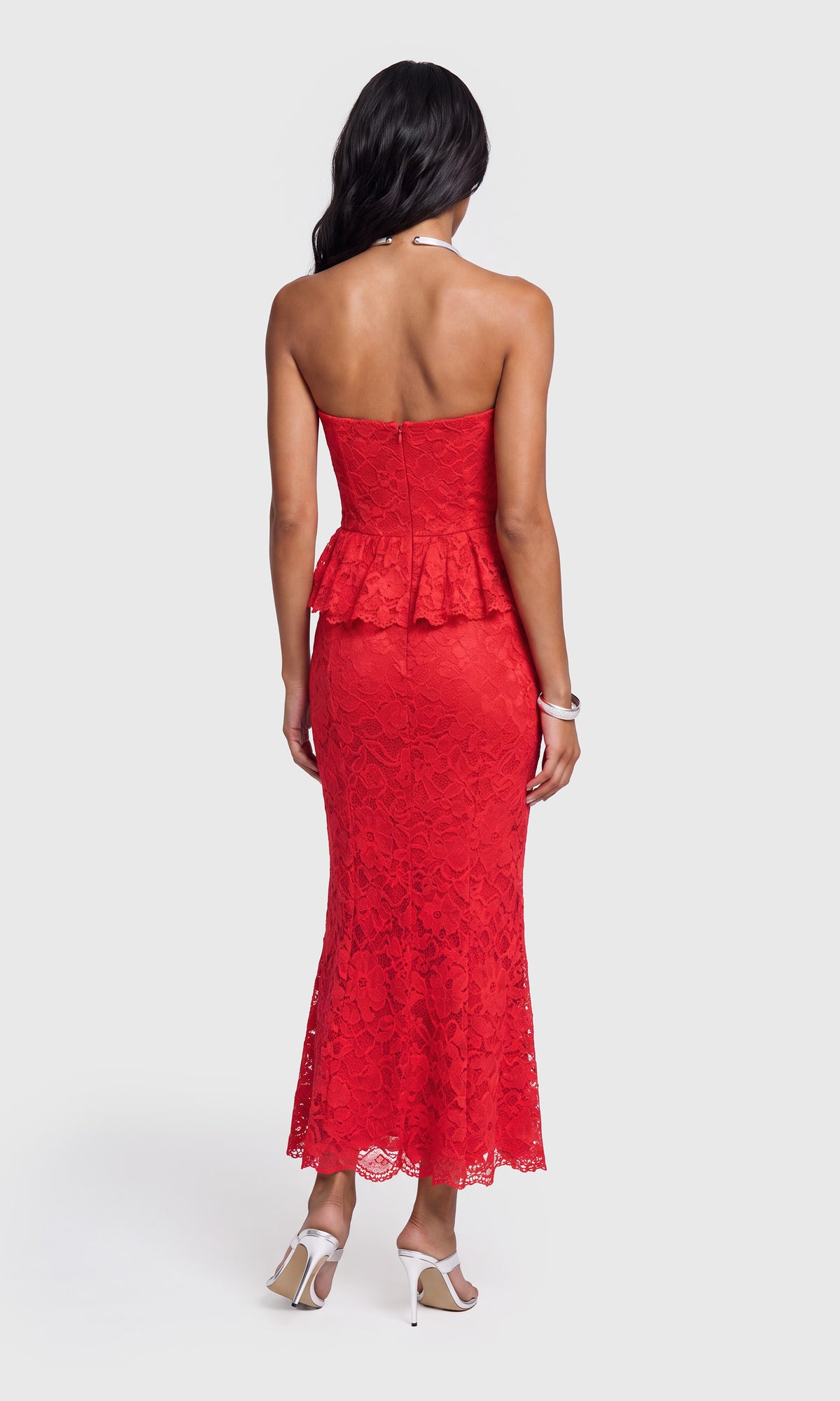 Back view of model wearing a bright red strapless lace maxi dress with a peplum waist, paired with white heeled sandals.