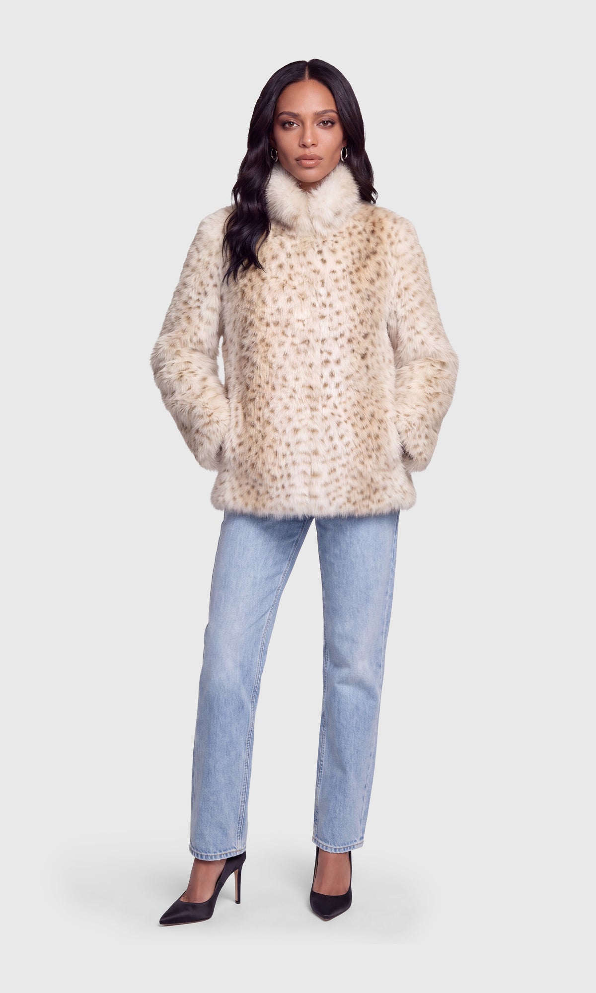 A woman modeling a beige faux fur jacket with a subtle brown leopard print pattern, paired with light blue jeans and black heels.