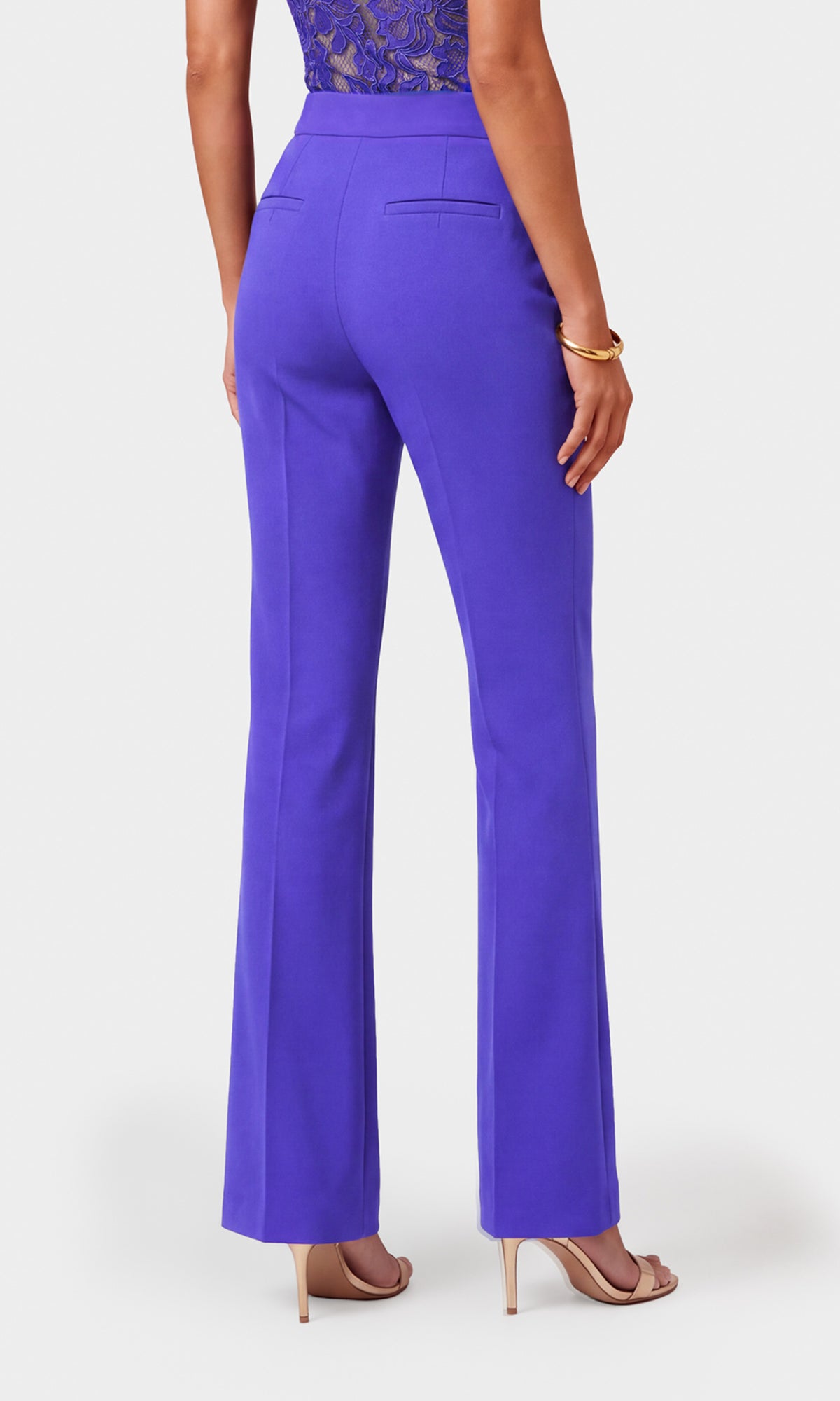 A model shown from the back wearing bright purple high-waisted flared trousers, paired with a purple lace bodysuit top.