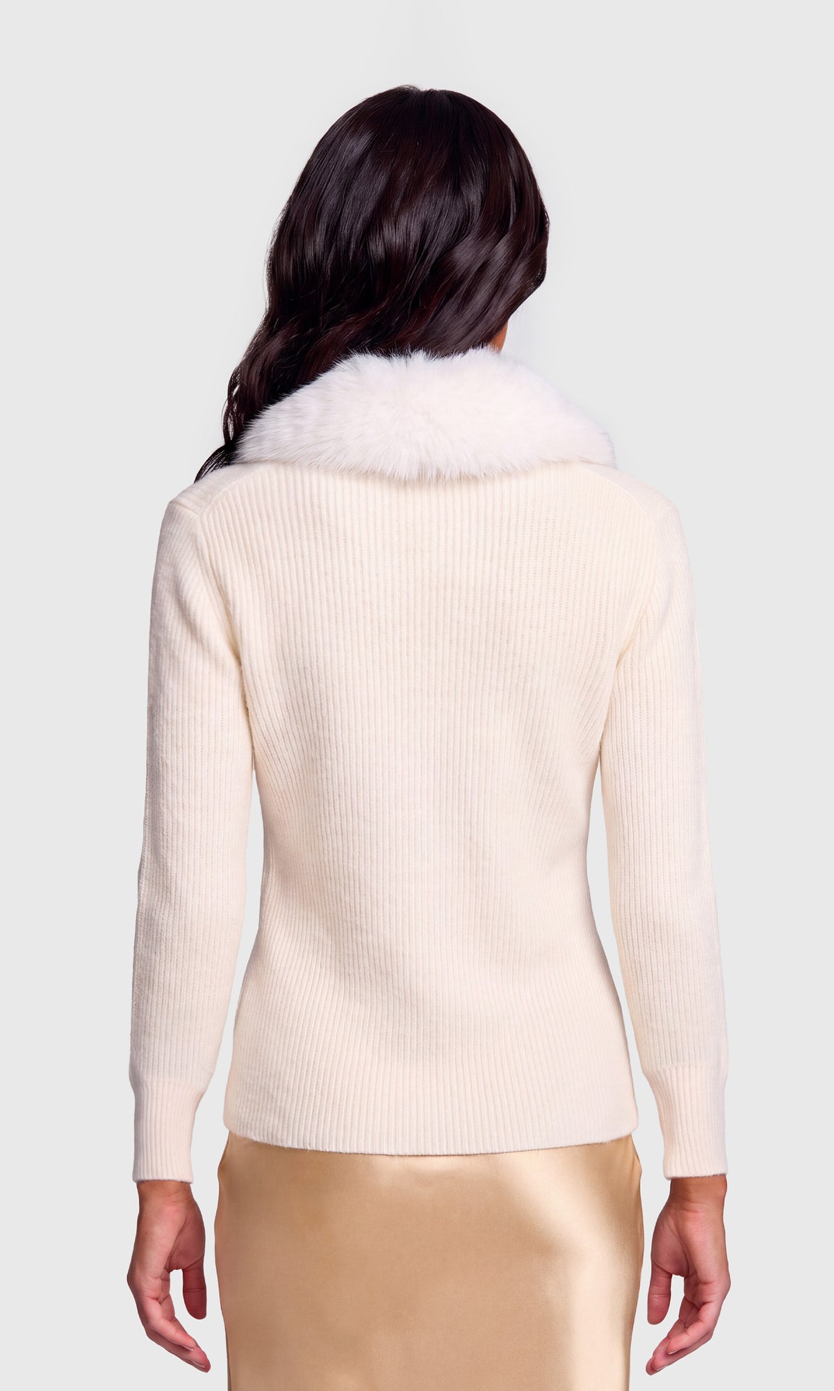 Back view of model wearing a cream ribbed knit sweater with a fluffy white fur collar, paired with a metallic gold skirt.