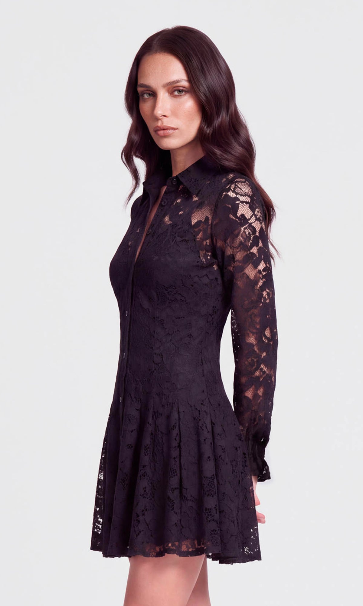 Side view of a woman modeling a black lace long-sleeve mini dress with a collared neckline and a fitted flared skirt.