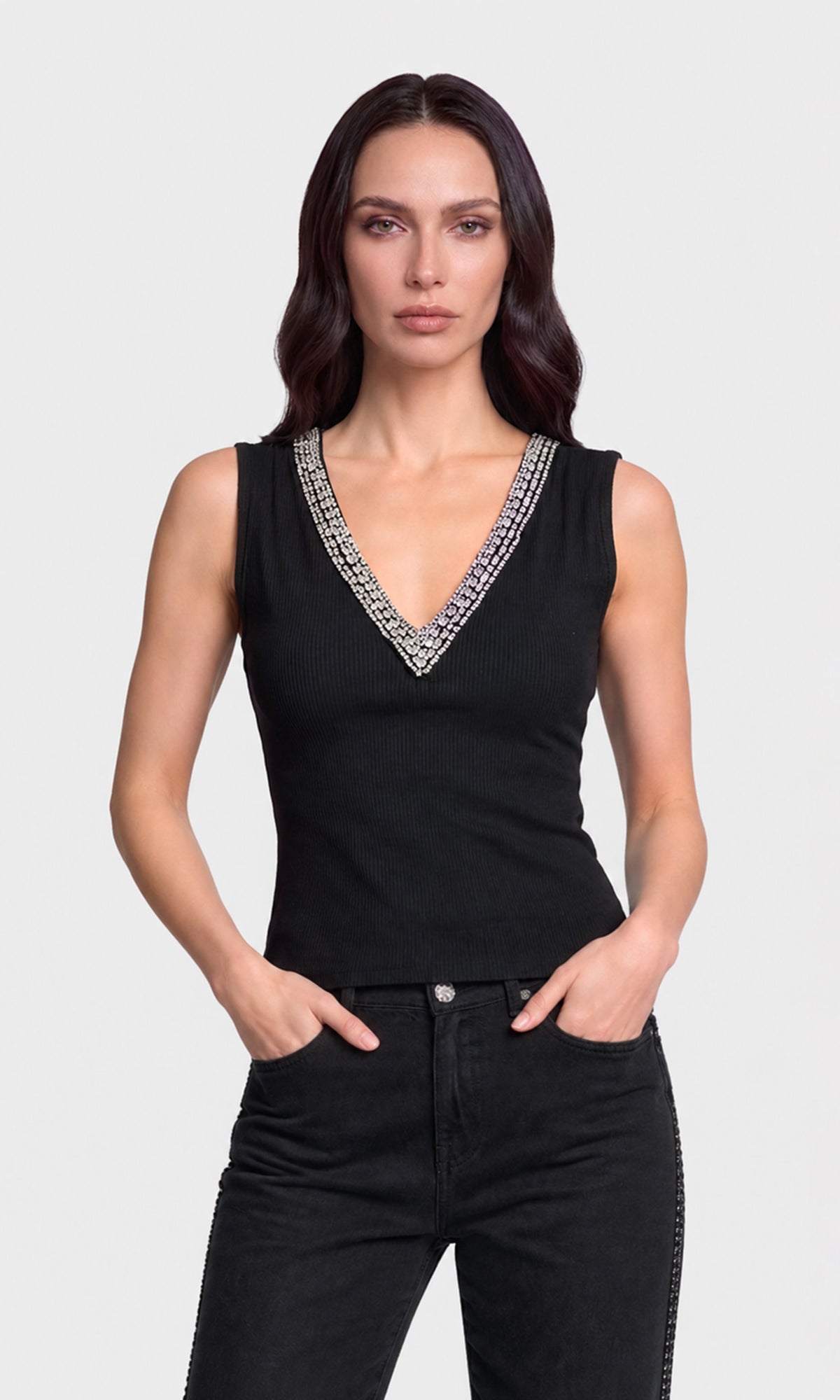 Model wearing a black sleeveless V-neck top with a silver rhinestone-trimmed neckline, paired with black jeans.