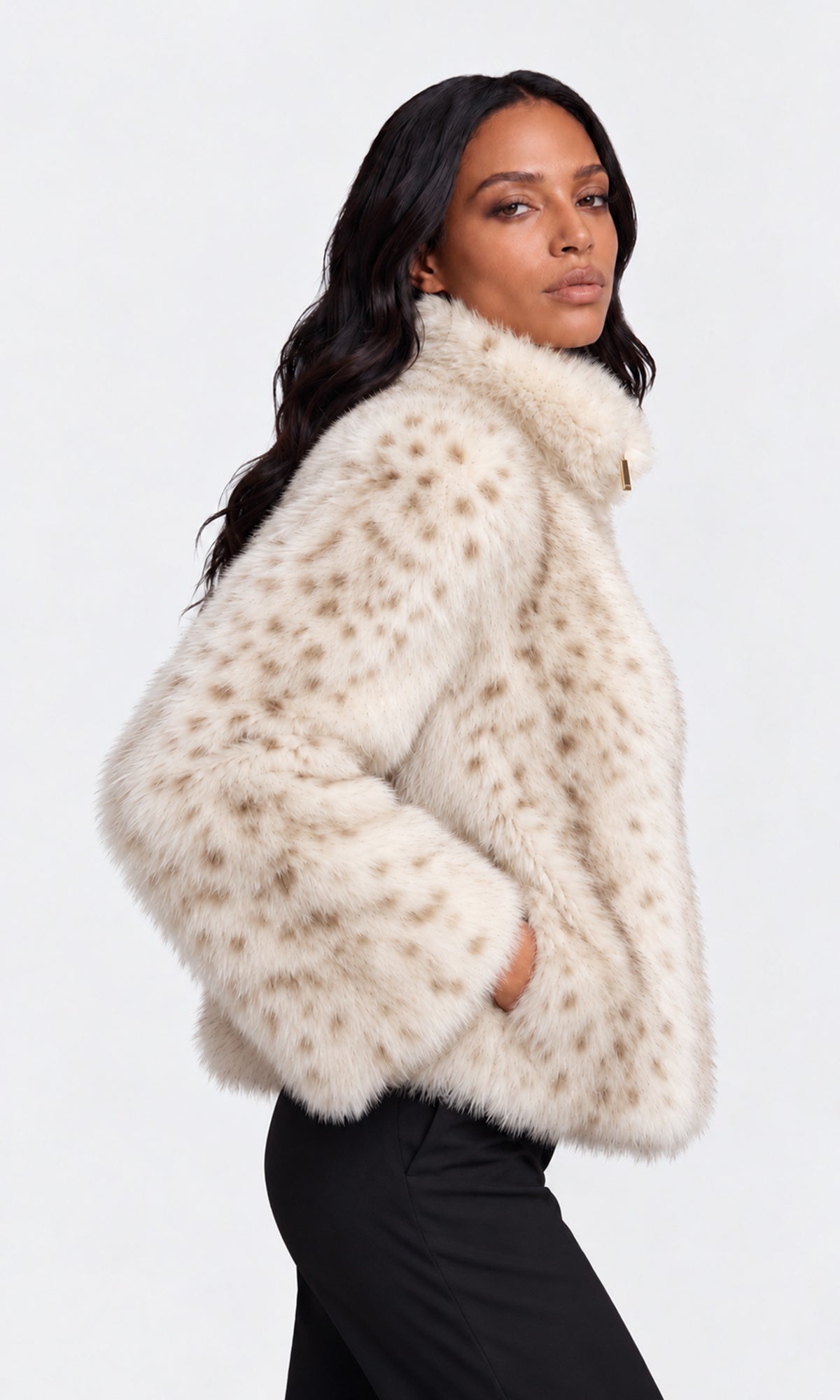 A woman wearing a cream faux fur jacket with brown spots, paired with black pants.
