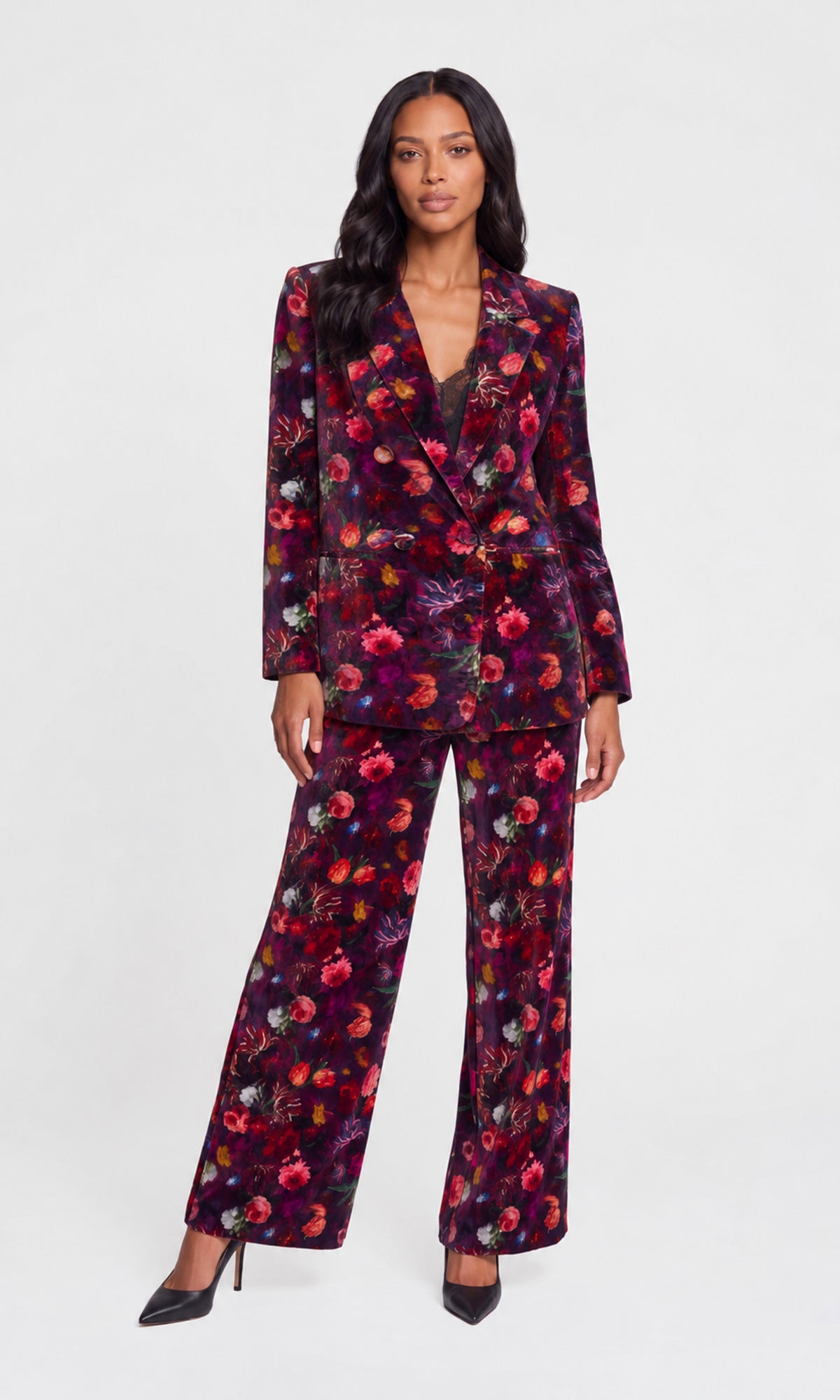 A woman modeling a matching floral velvet pantsuit with a deep V-neck blazer and wide-leg trousers, styled with black pointed-toe heels.