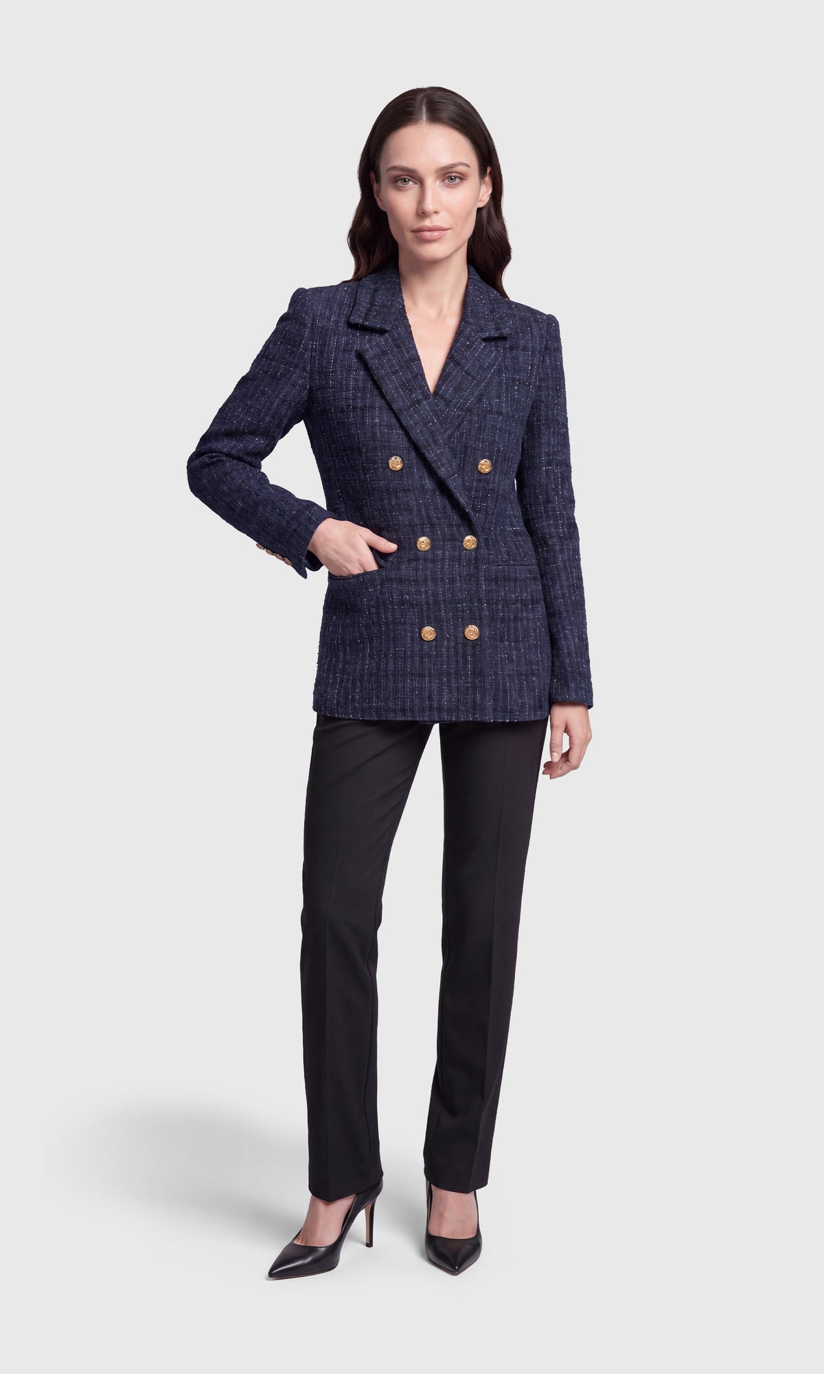 A woman modeling a navy blue double-breasted blazer with a subtle plaid pattern and gold buttons, paired with black trousers and black heels.
