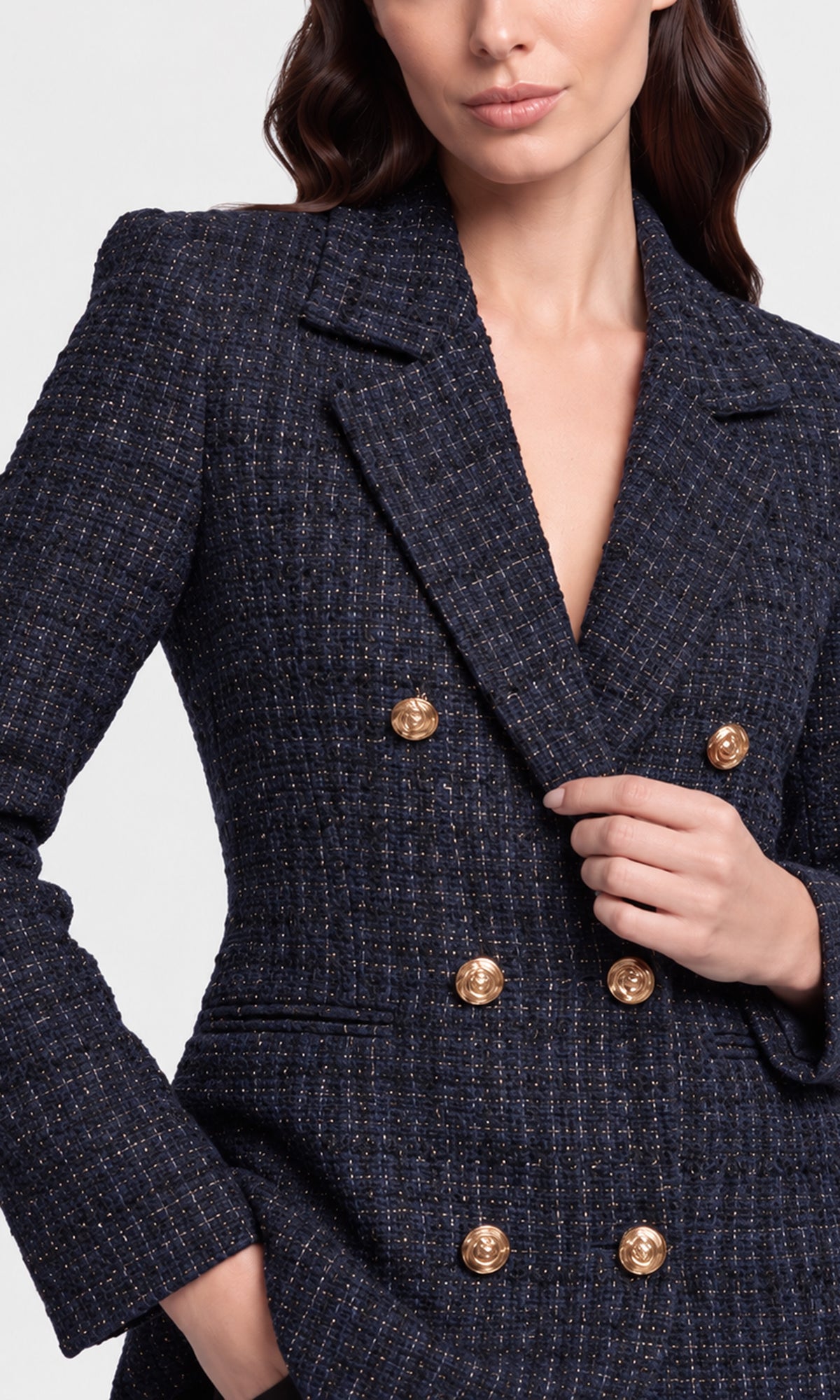 A close-up of a model wearing a navy blue tweed double-breasted blazer with prominent gold buttons.