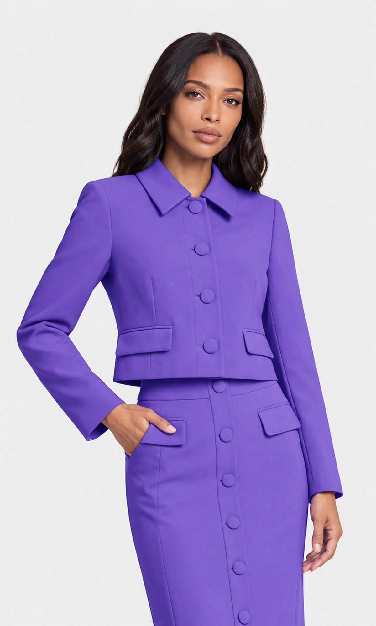 A woman modeling a vibrant purple two-piece suit consisting of a cropped button-front jacket with a pointed collar and a matching high-waisted pencil skirt with a button-front closure.
