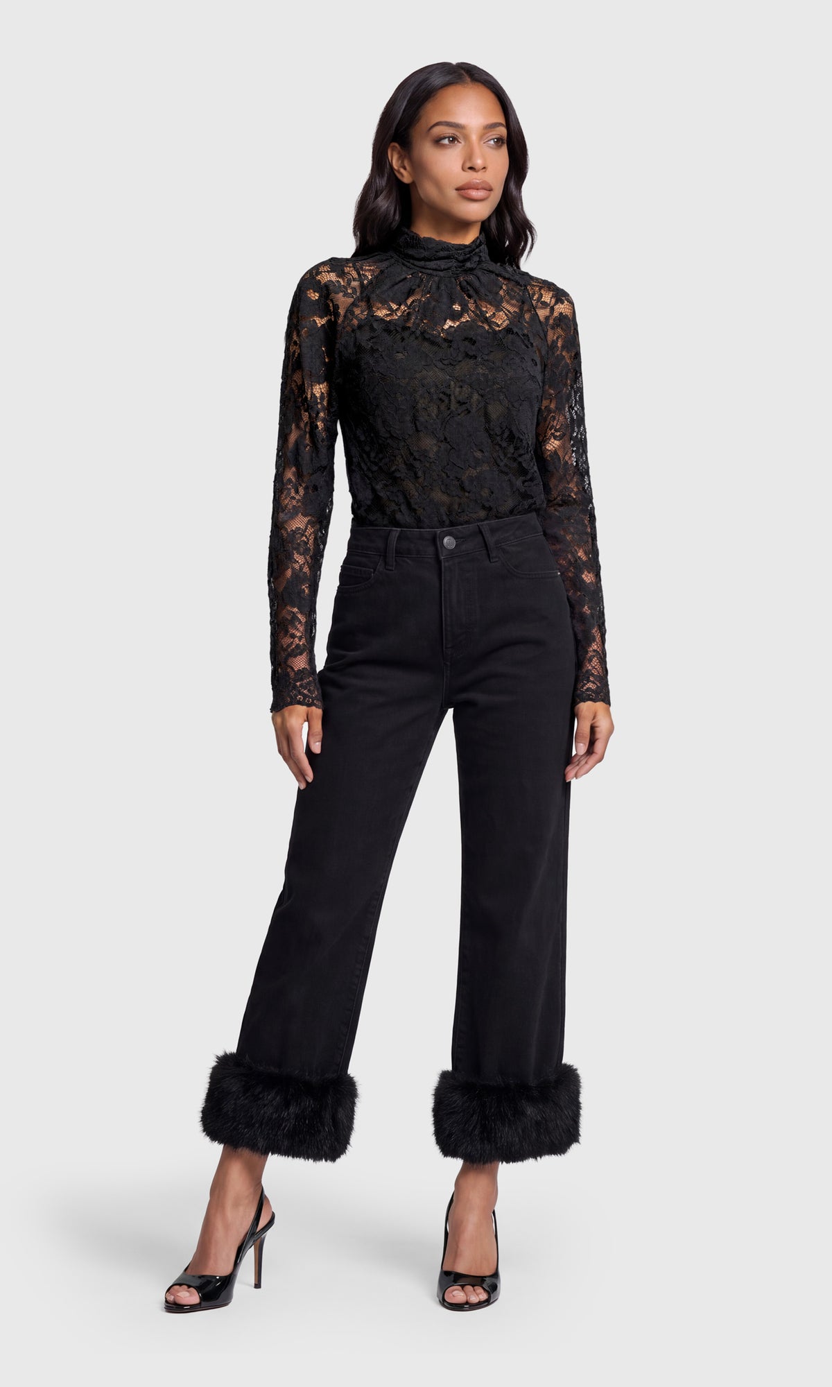 Model wearing a black lace, mock-neck top with black jeans and black open-toe heels.