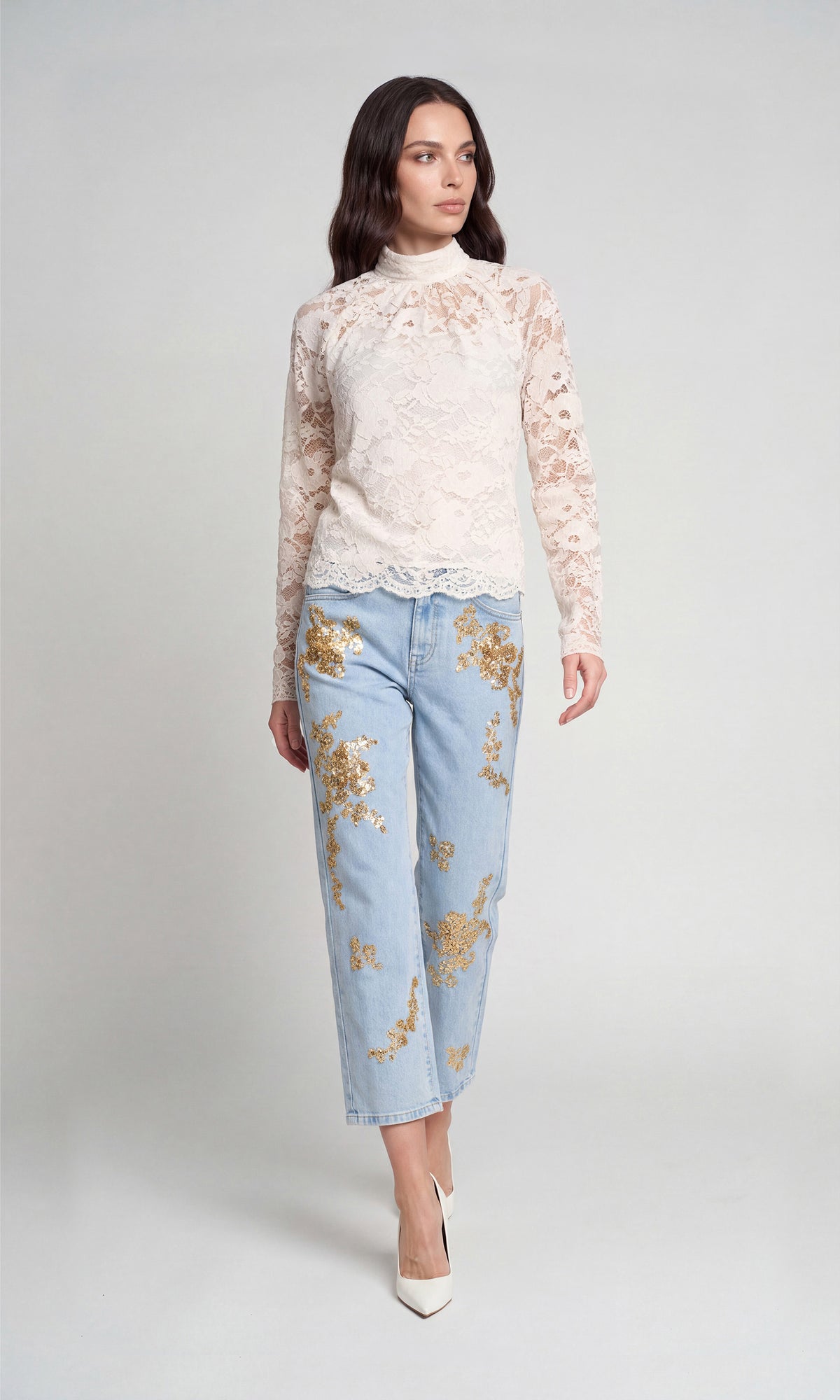 Model wearing a cream lace mock-neck long-sleeve top, light-wash blue cropped jeans with gold floral embroidery, and white pointed-toe heels.