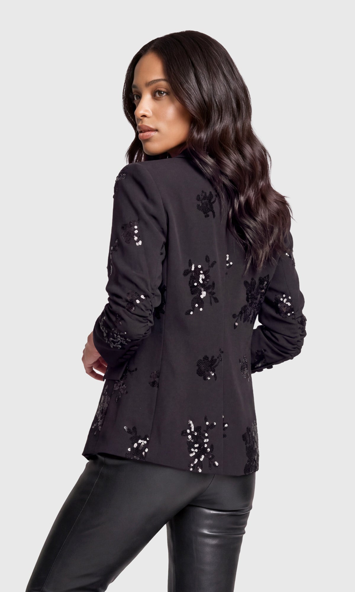 Back view of model wearing a black long-sleeve blazer with silver sequin floral embroidery.