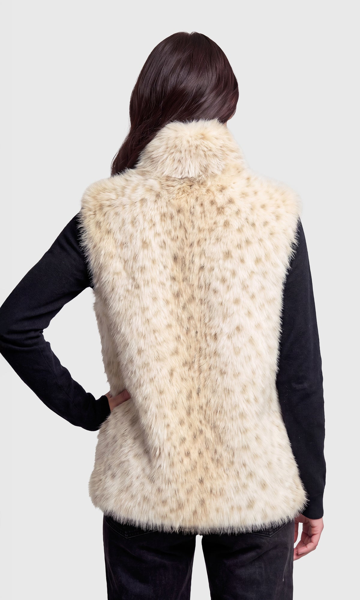 Back view of model wearing a sleeveless faux fur vest with a beige and cream leopard-like pattern, worn over a black long-sleeve top.