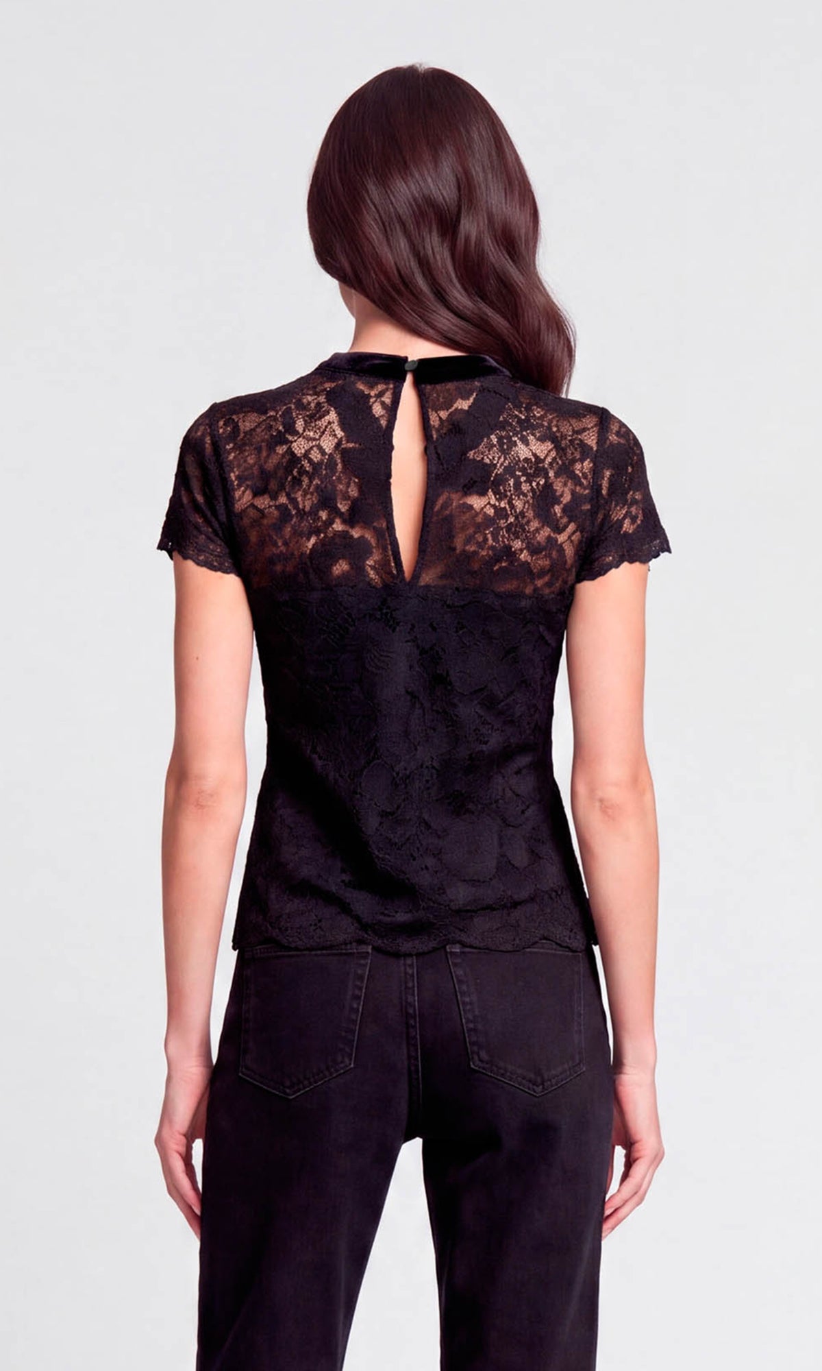 A woman viewed from the back wearing a black lace short-sleeve top with a keyhole cutout and black pants.