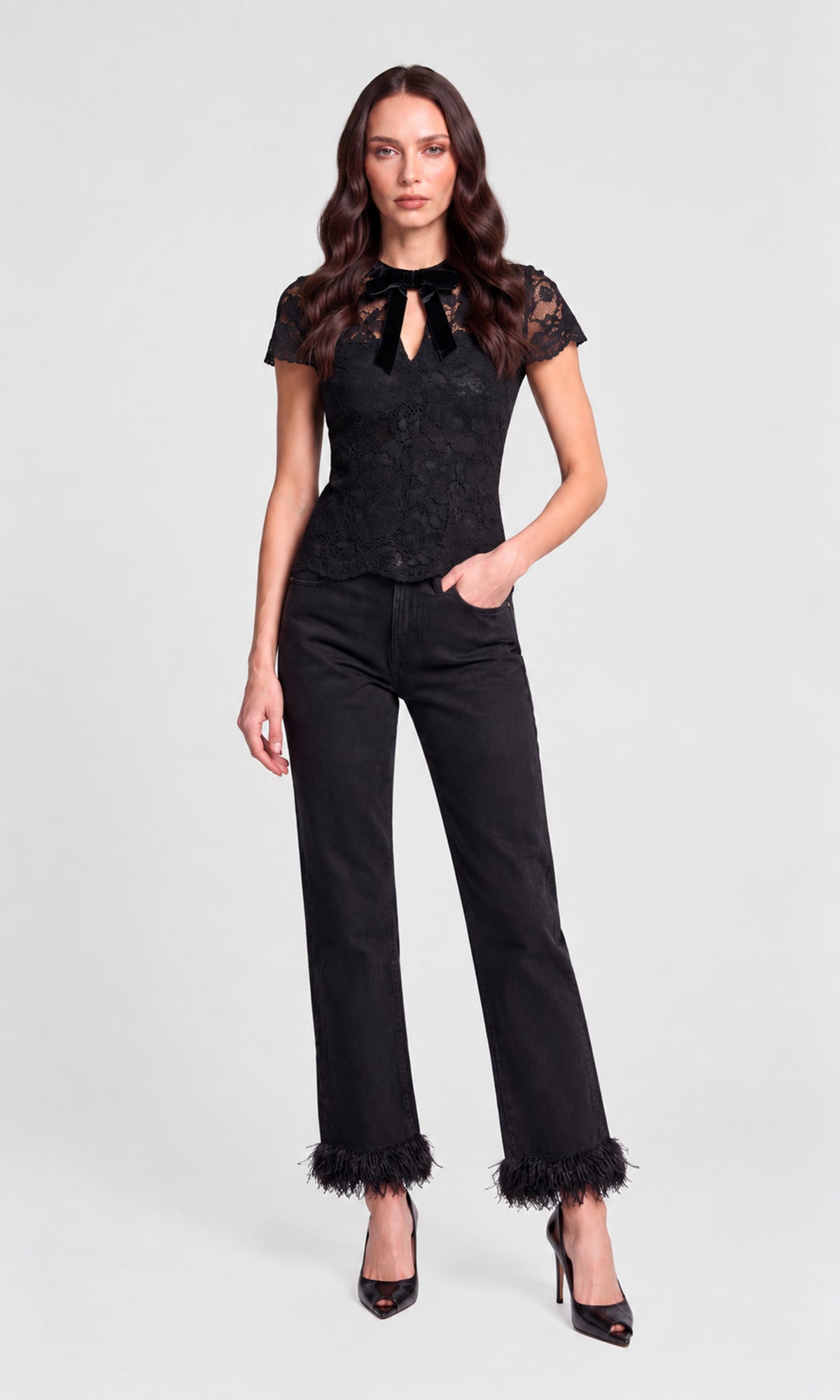 A woman modeling a black lace short-sleeve top with a keyhole cutout and black wide-leg jeans with feathered cuffs, paired with black high heels, against a light gray studio background.