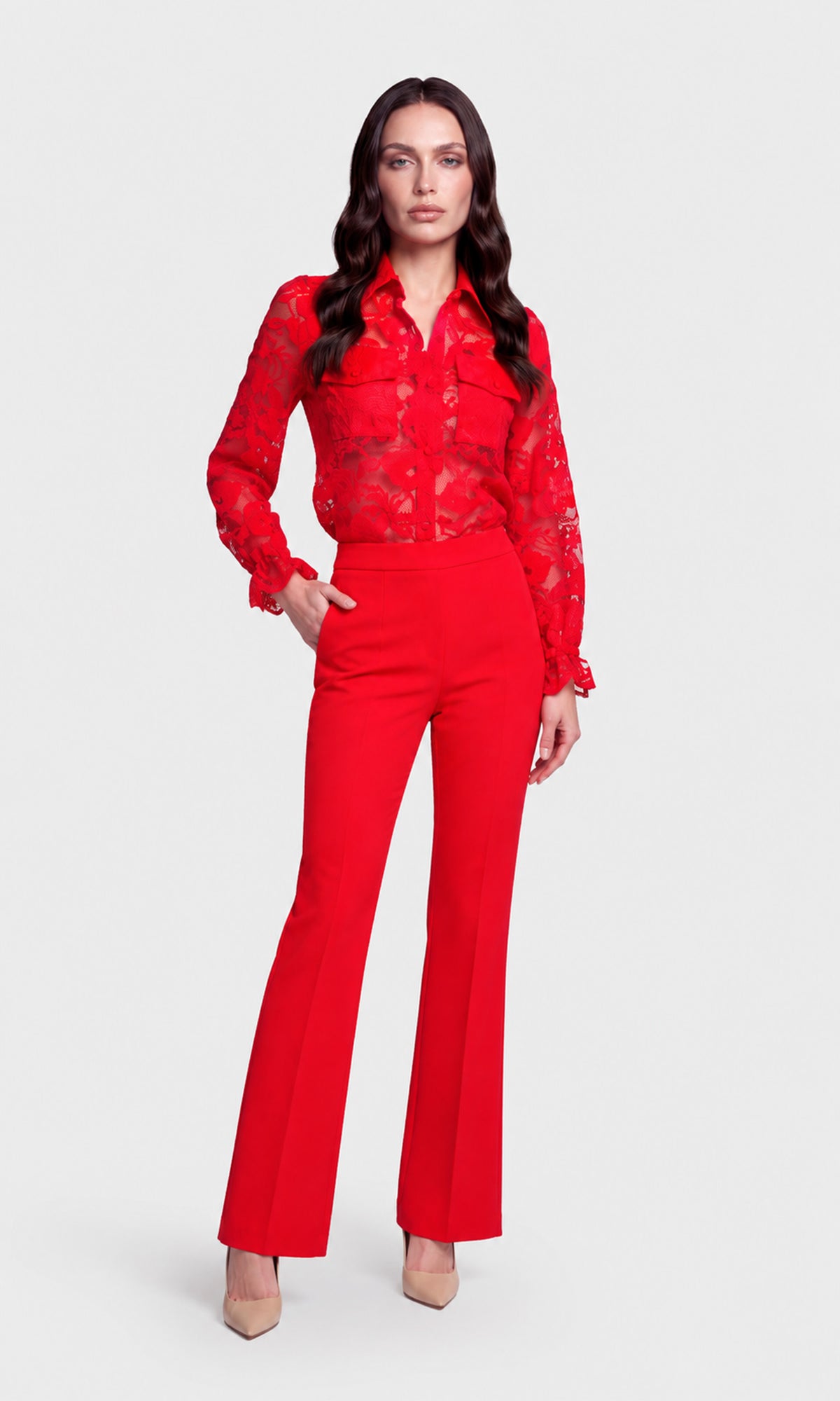 A woman modeling a red two-piece outfit consisting of a sheer floral long-sleeve button-up shirt and matching high-waisted red flare pants.
