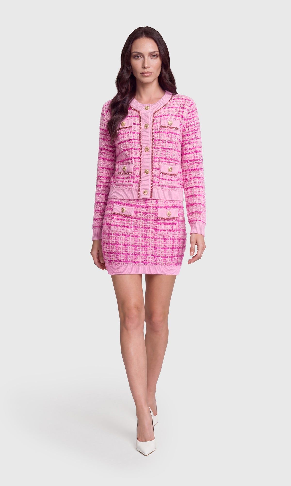 A woman models a pink tweed jacket and matching mini skirt set with gold buttons.