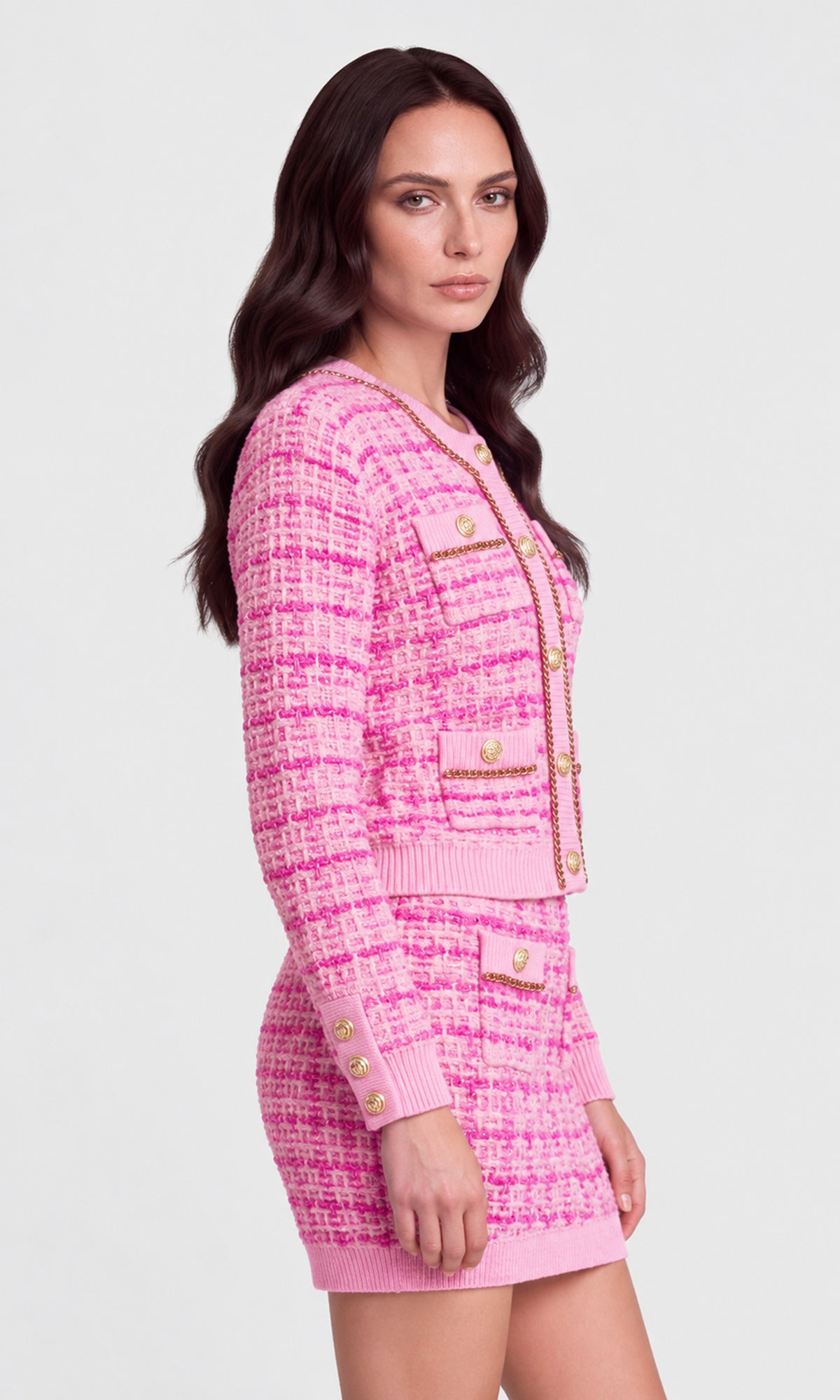 A woman modeling a pink tweed cardigan and matching mini skirt set with gold-tone buttons and trim.