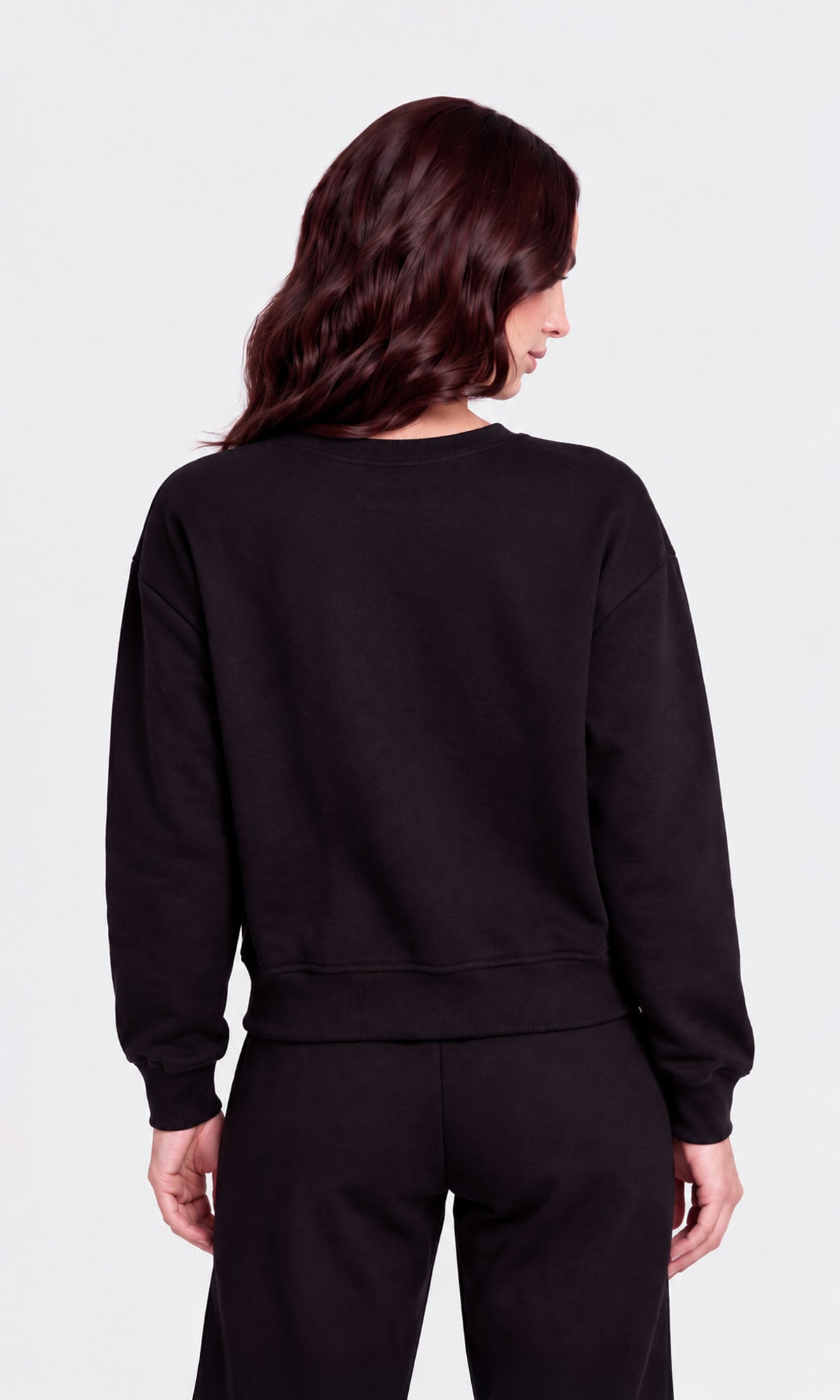 Back view of model wearing a black crewneck sweatshirt and matching black sweatpants.