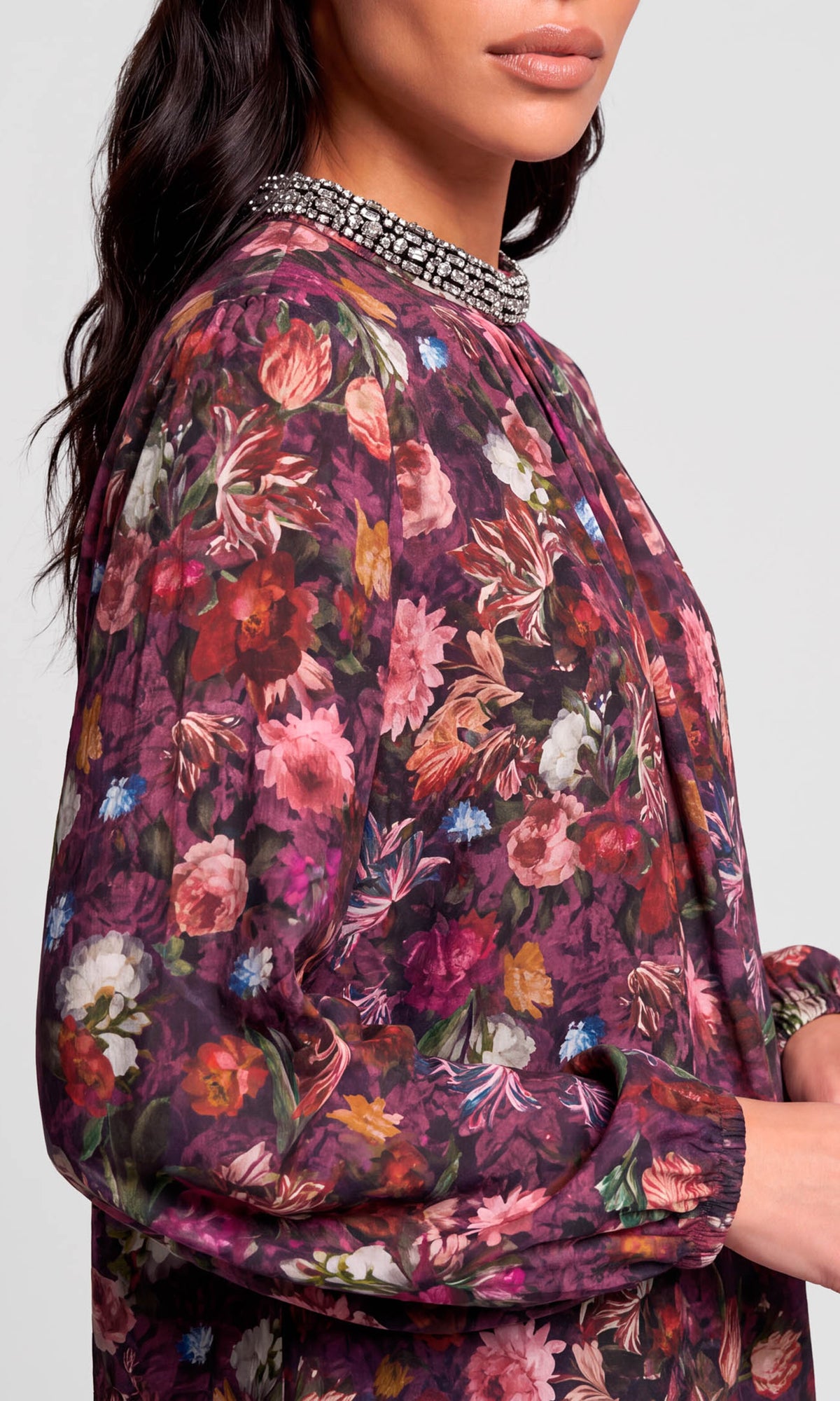 A close-up of a woman wearing a long-sleeve floral blouse with a beaded embellished collar.