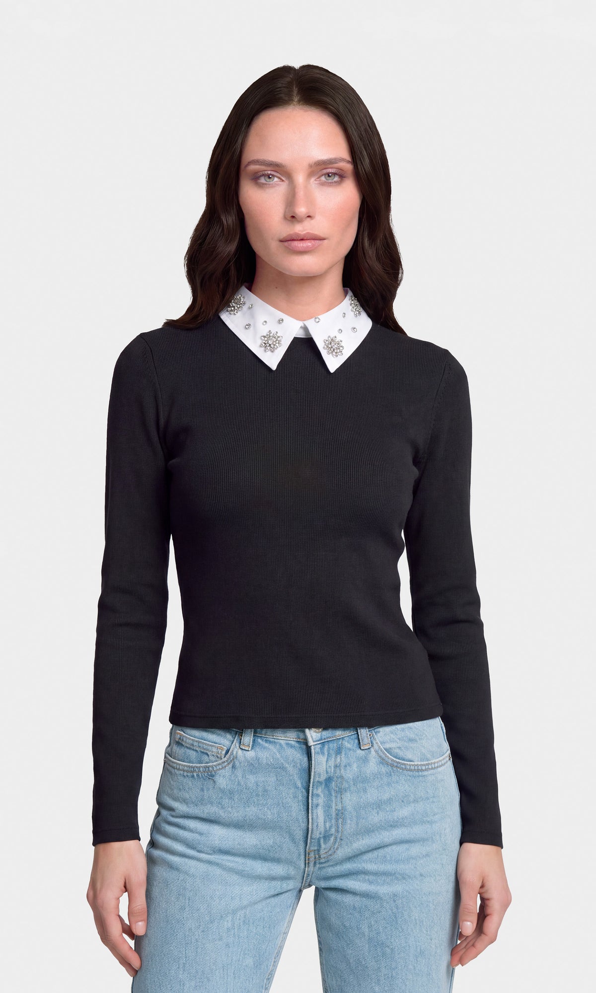Model wearing a black long-sleeve knit sweater with a contrasting white pointed collar decorated with small silver floral motifs, paired with light blue jeans.