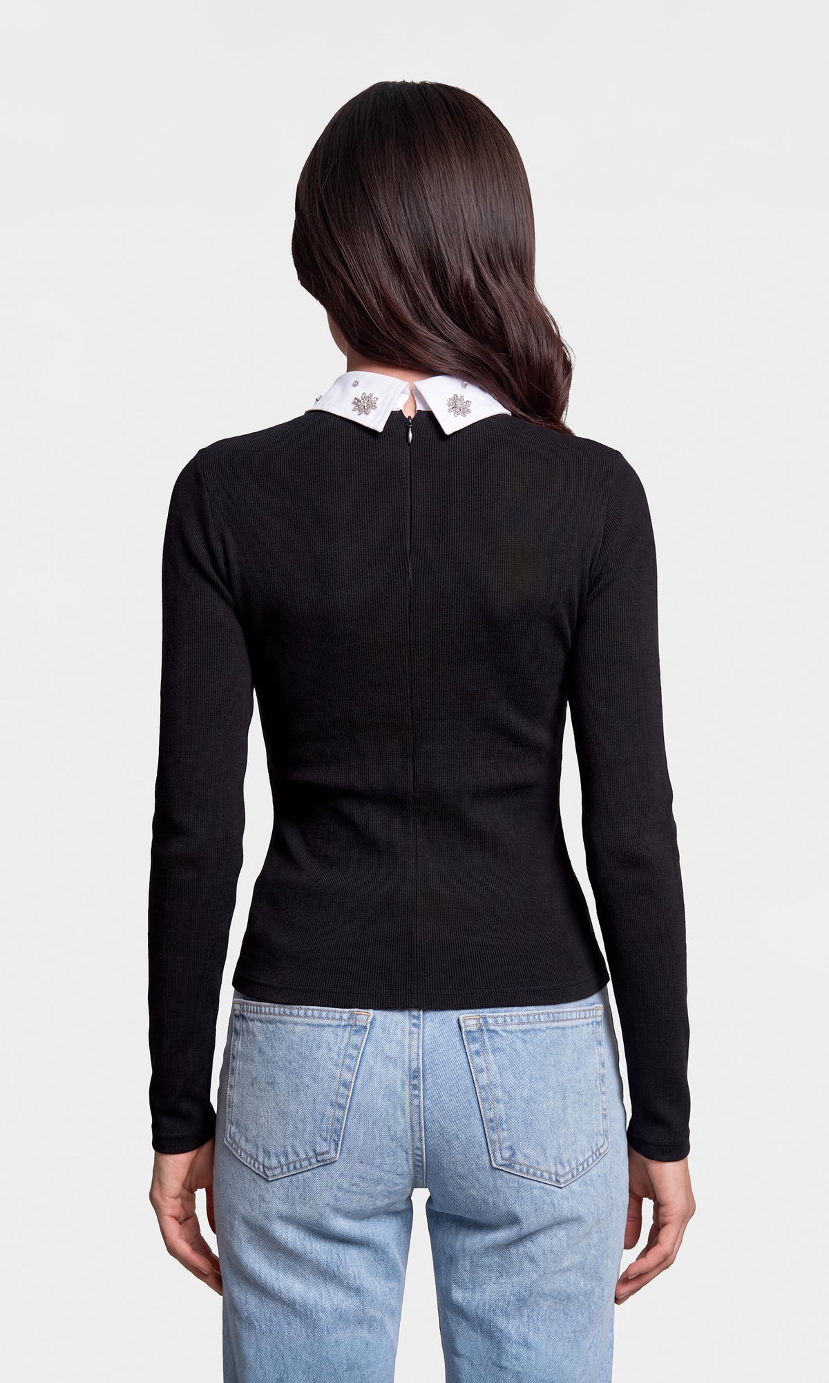 Back view of model wearing a fitted black long-sleeve top with a contrasting white pointed collar featuring small crystal details, paired with light blue jeans.