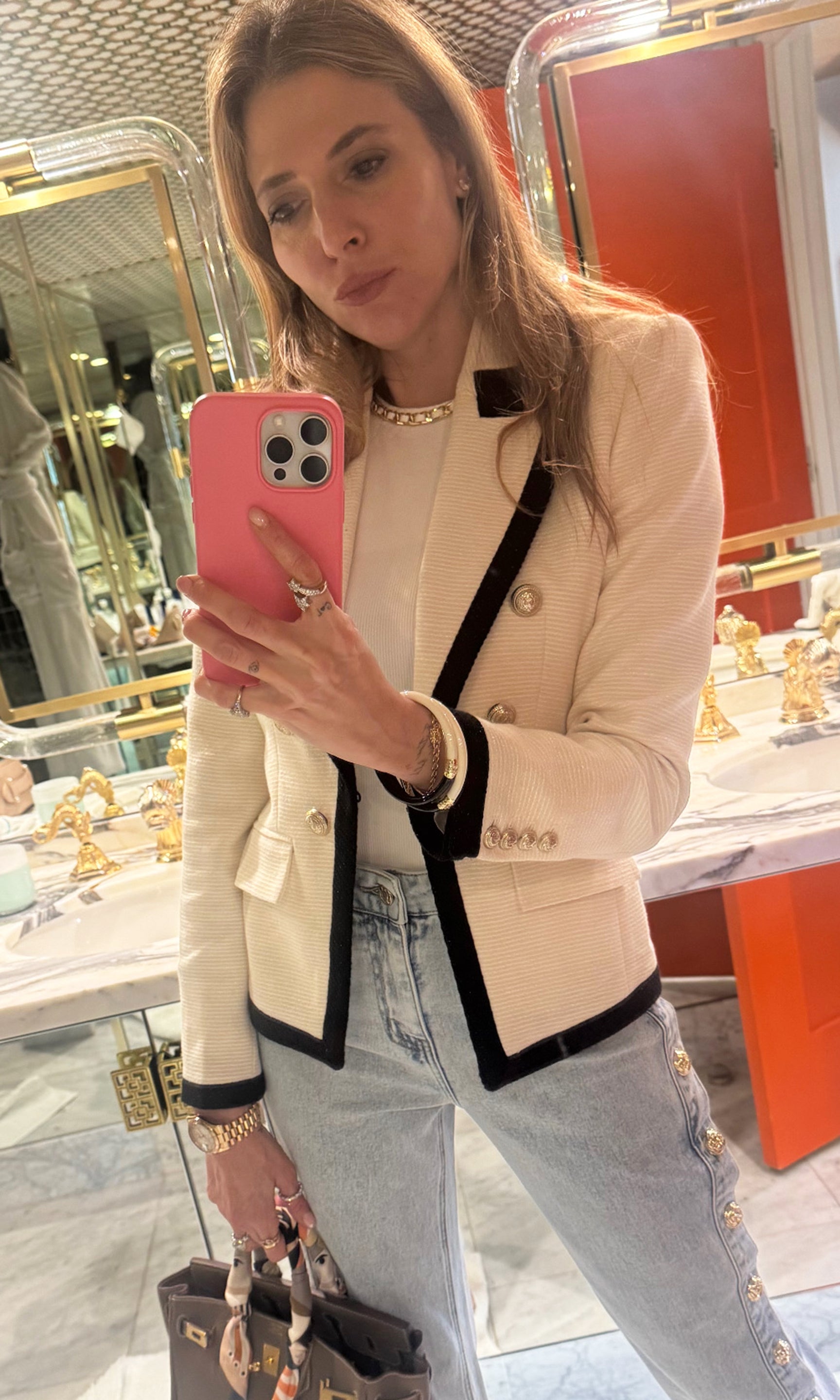 Our founder Roni taking a mirror selfie wearing a white blazer with black contrast.