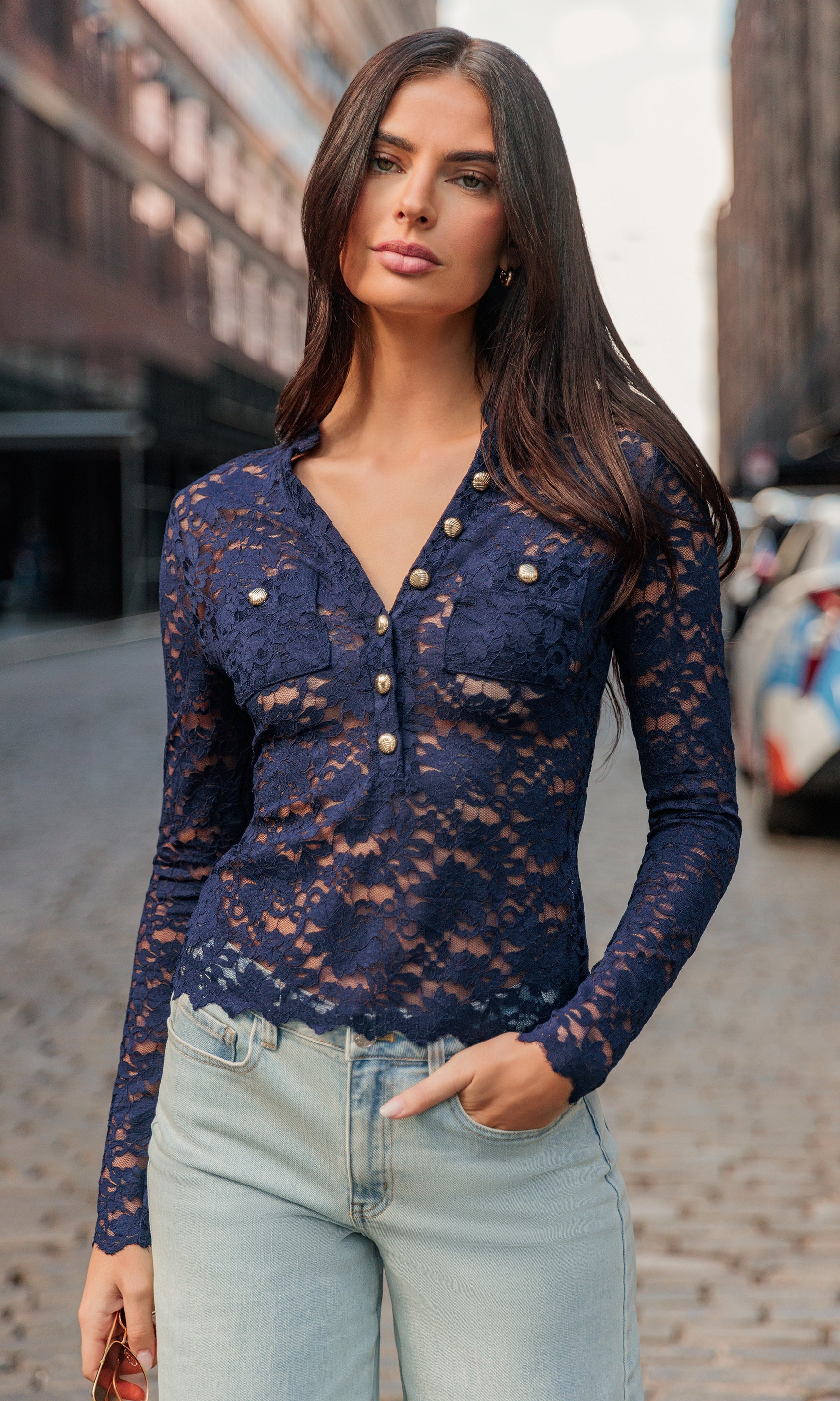 Woman wearing a navy lace long-sleeve top and light blue jeans on a city street.