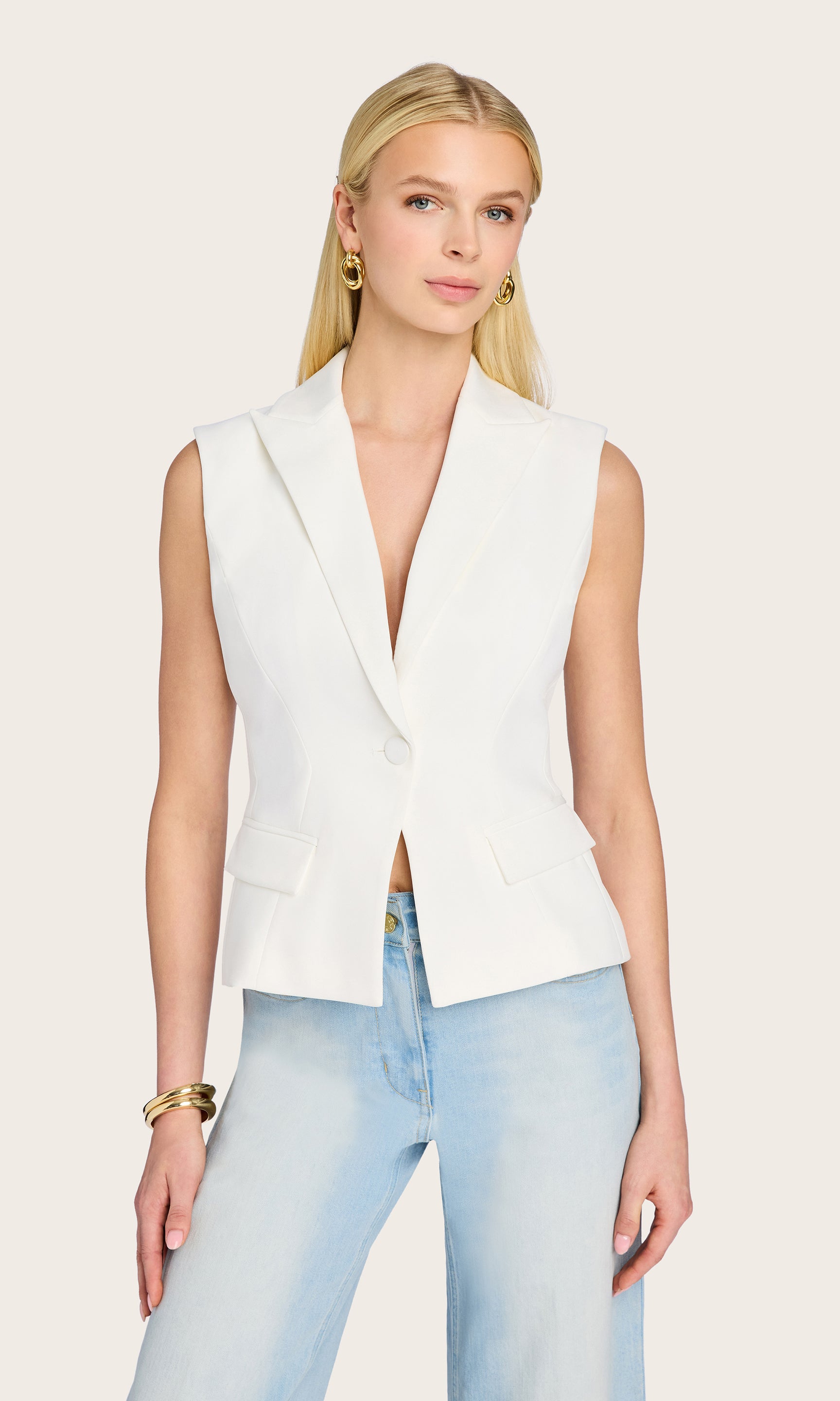 The model wears the Jenna Sleeveless Blazer in a crisp front view, paired with light denim culottes to highlight the clean tailoring and single-breasted silhouette.