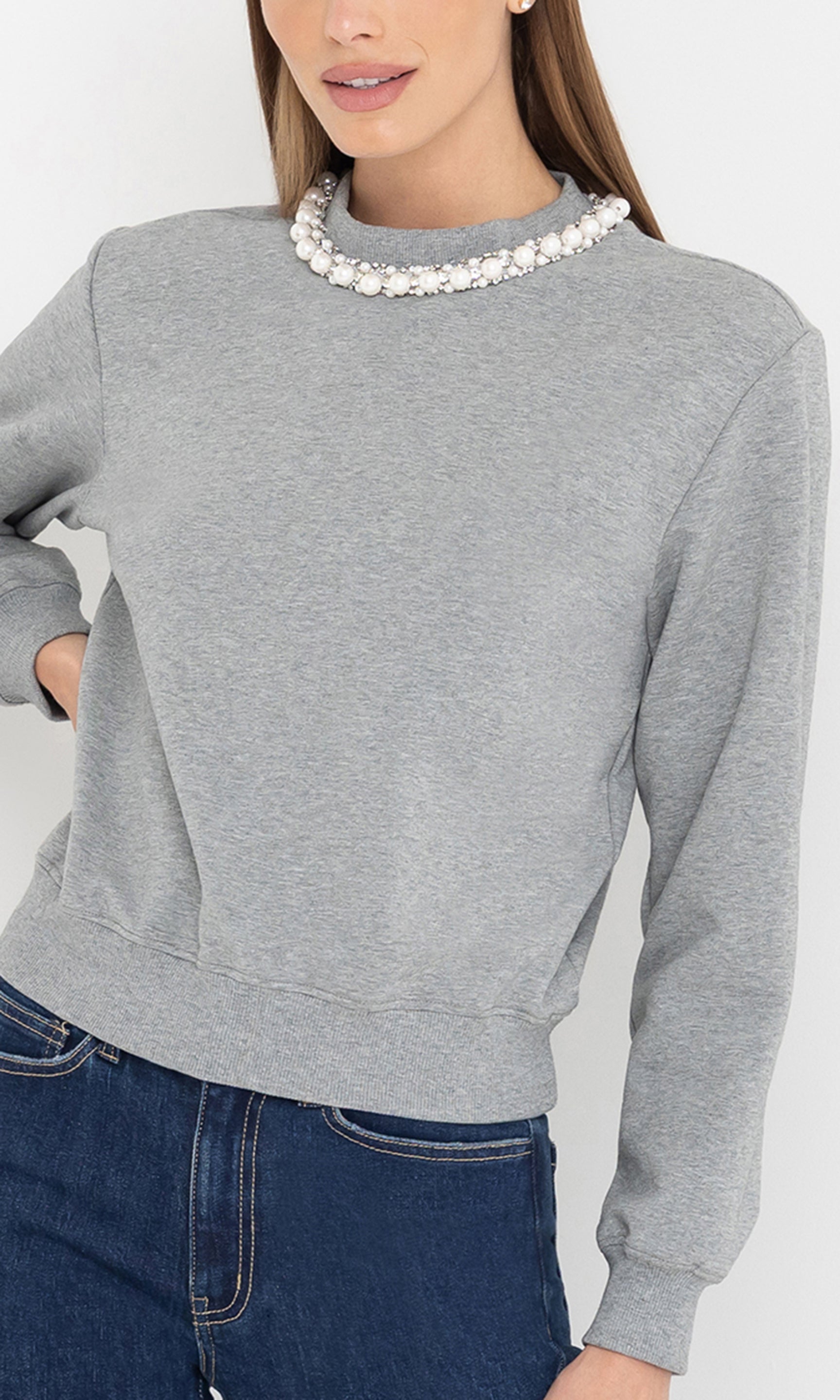Person wearing a gray sweatshirt and blue jeans with a white background