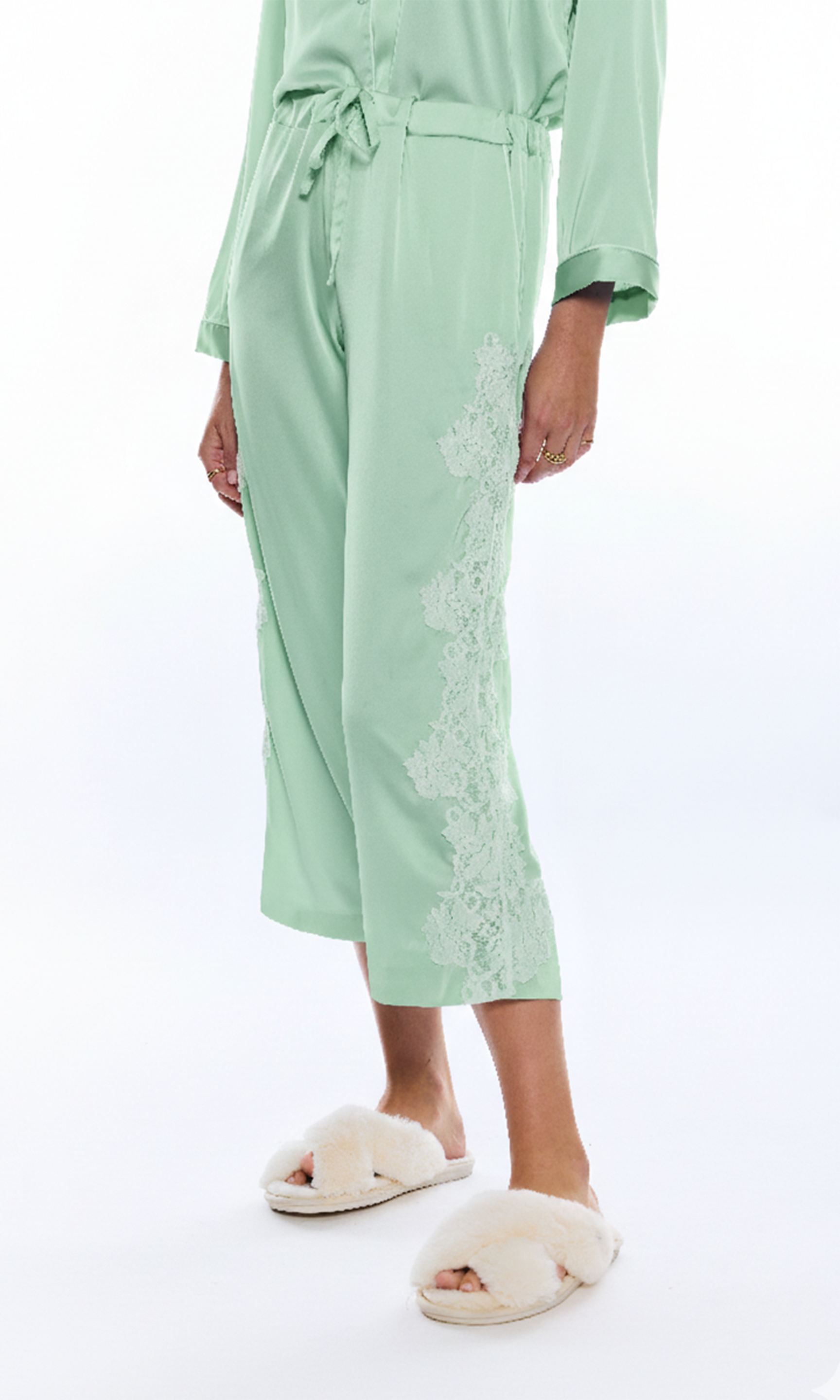 Person wearing a light green pajama pant with lace details on a white background