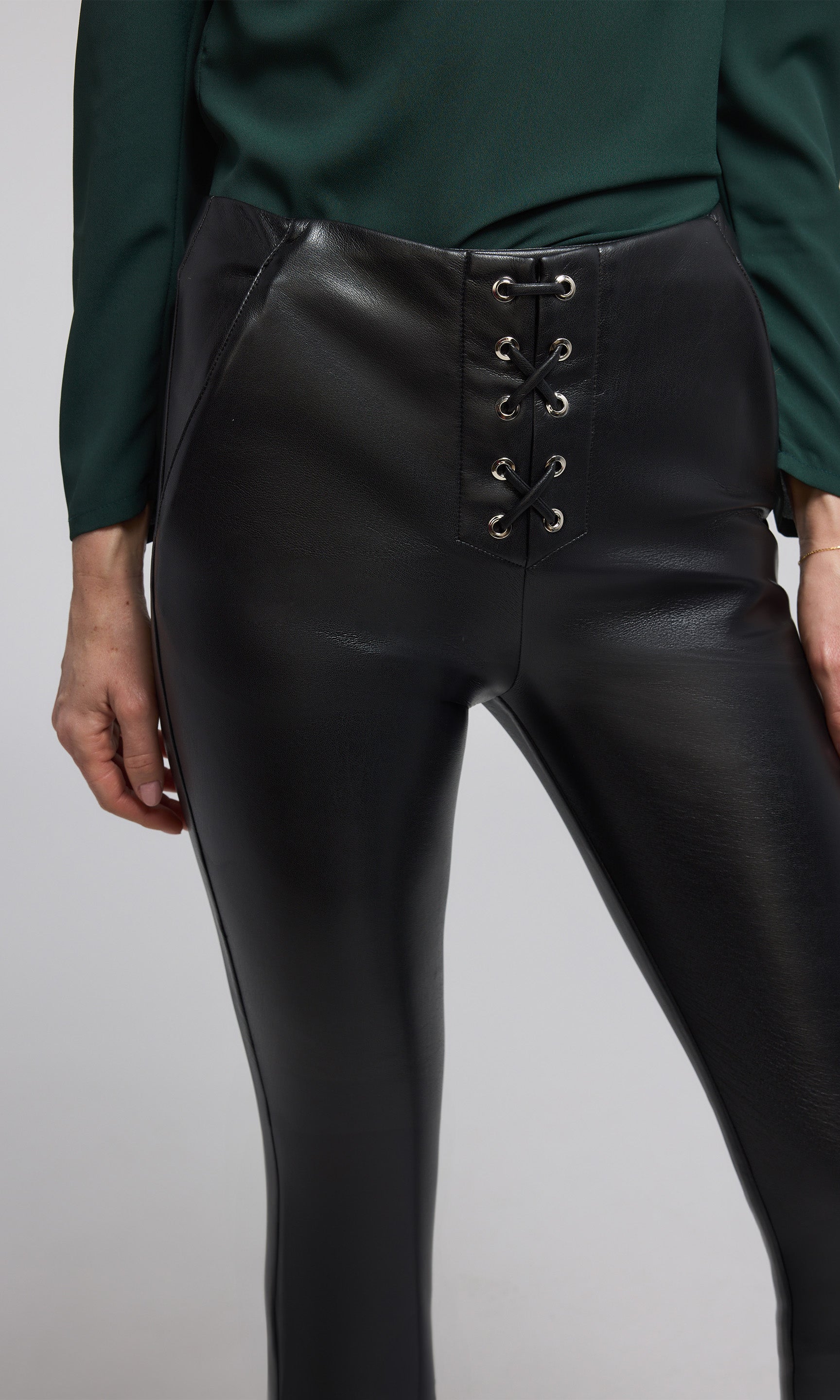 A model showcases vegan leather lace-up leggings featuring intricate lace detailing, emphasizing a stylish and edgy look.