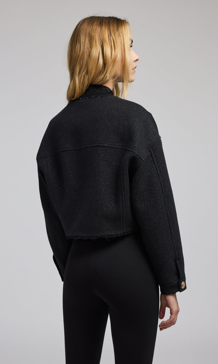 A stylish black cropped bomber jacket with gold buttons, emphasizing a modern and elegant look in outerwear fashion.