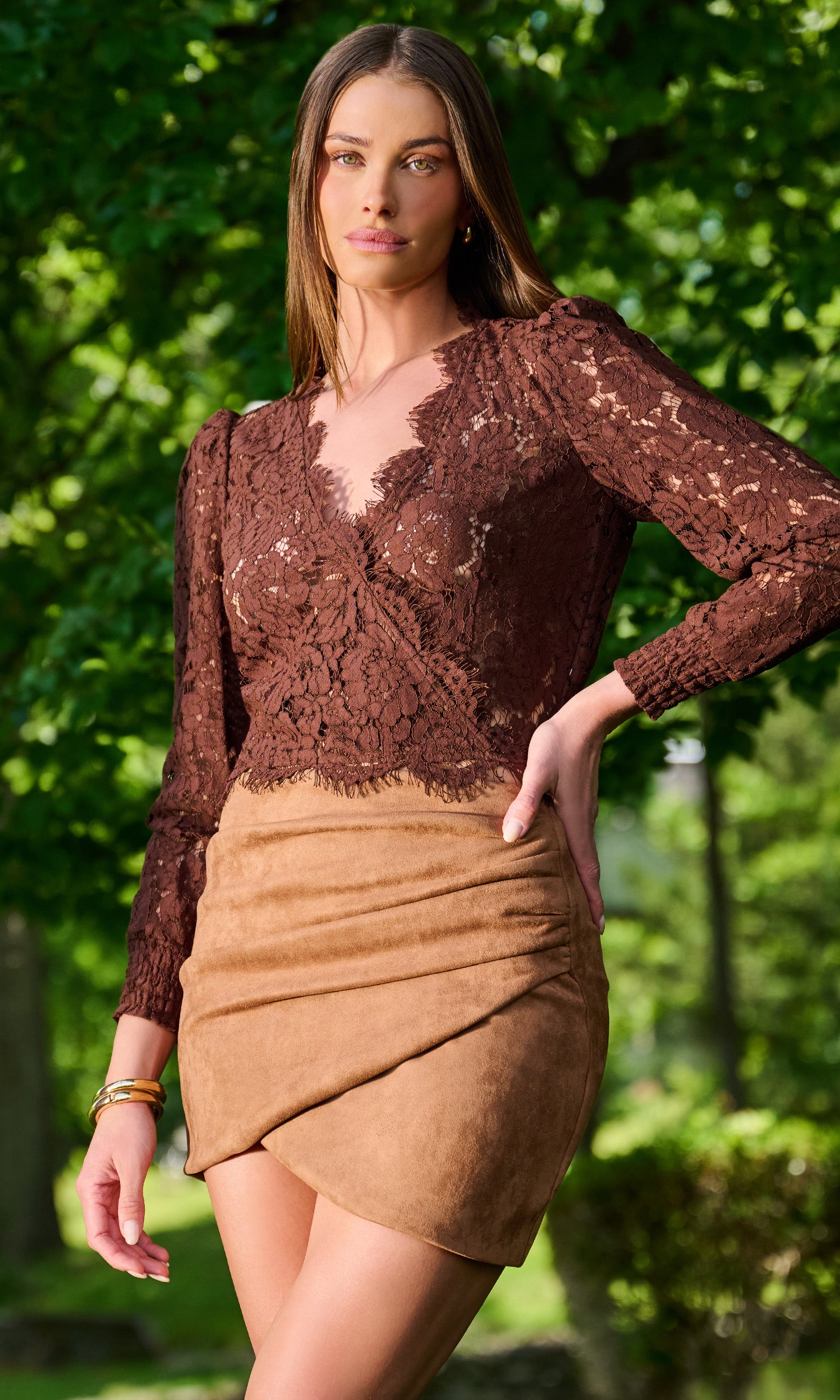Model wearing a brown lace long-sleeve top with a tan wrap-style skirt, photographed outdoors.
