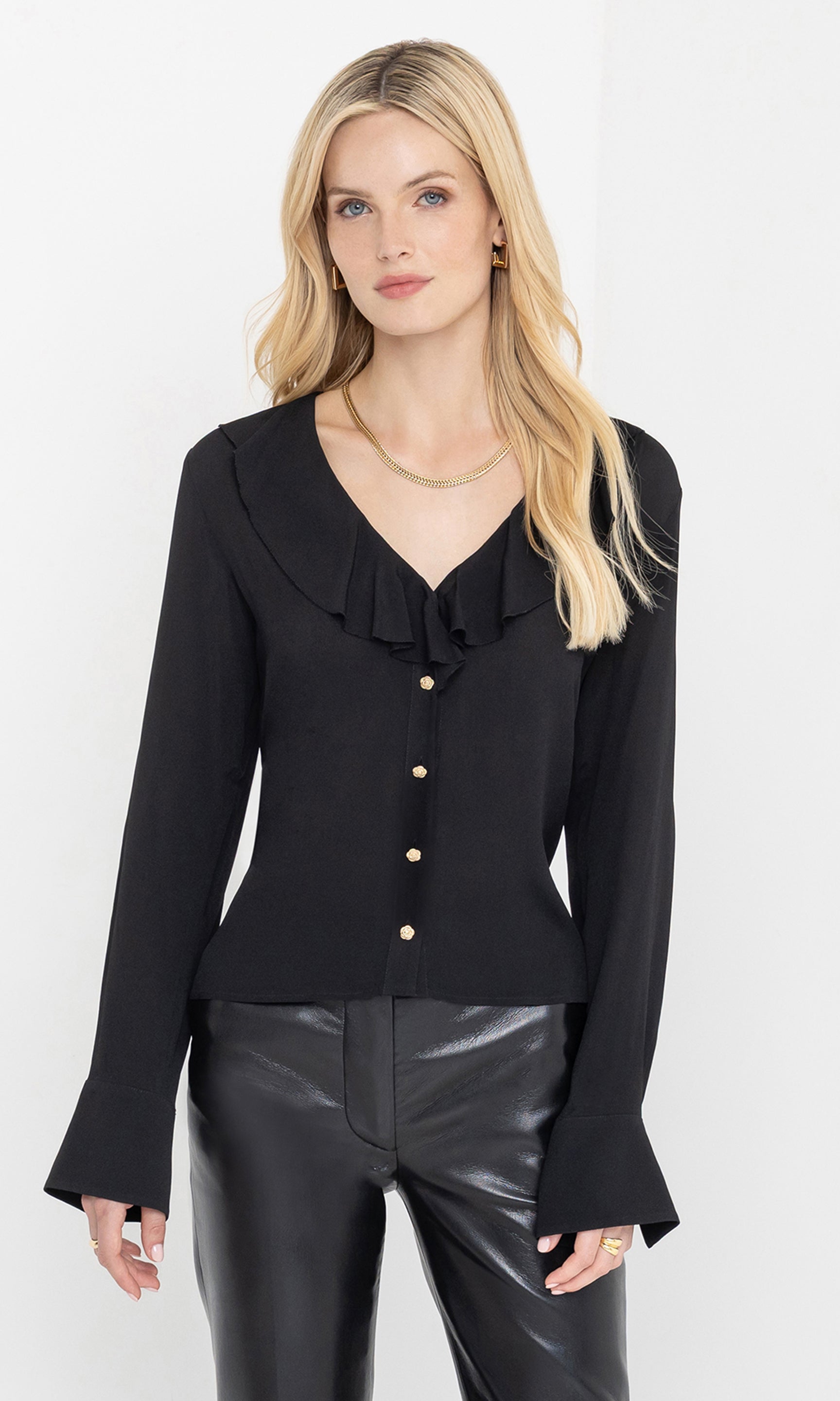 Woman wearing a black blazer with ruffled details and leather pants on a white background