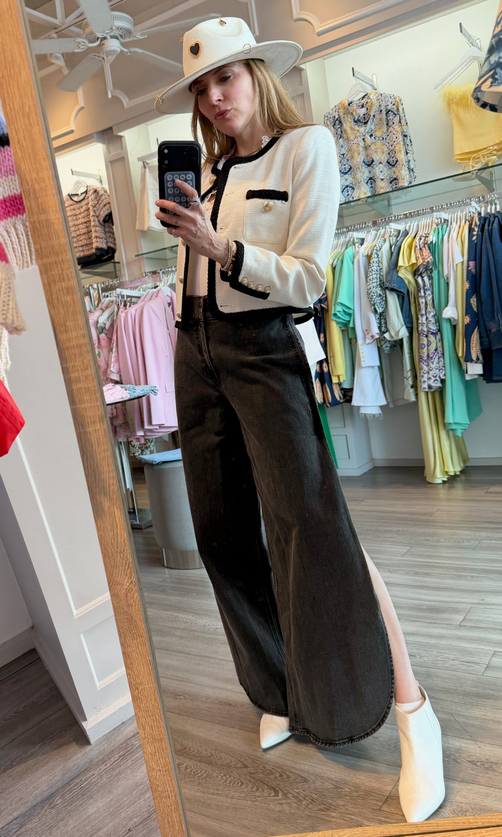 Founder Roni taking a mirror selfie in a clothing store, wearing a white blouse with black trim and dark pants.