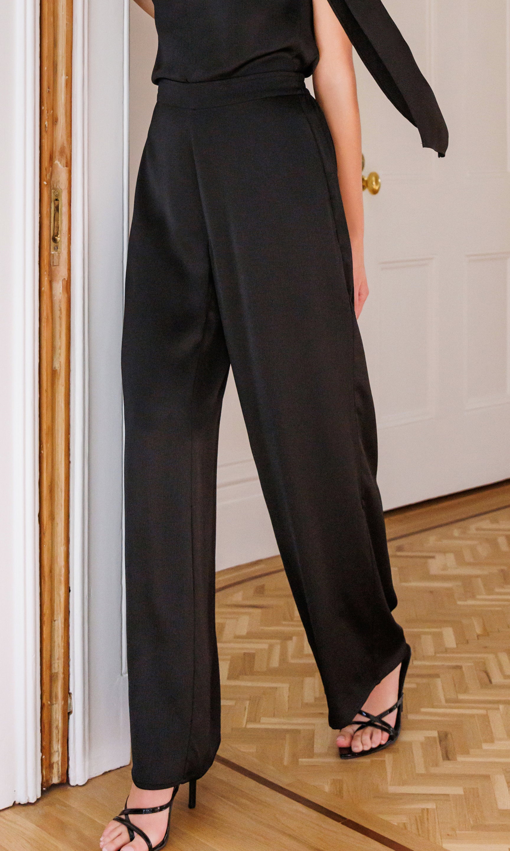 Person wearing black satin high-waisted pants and a black top indoors.