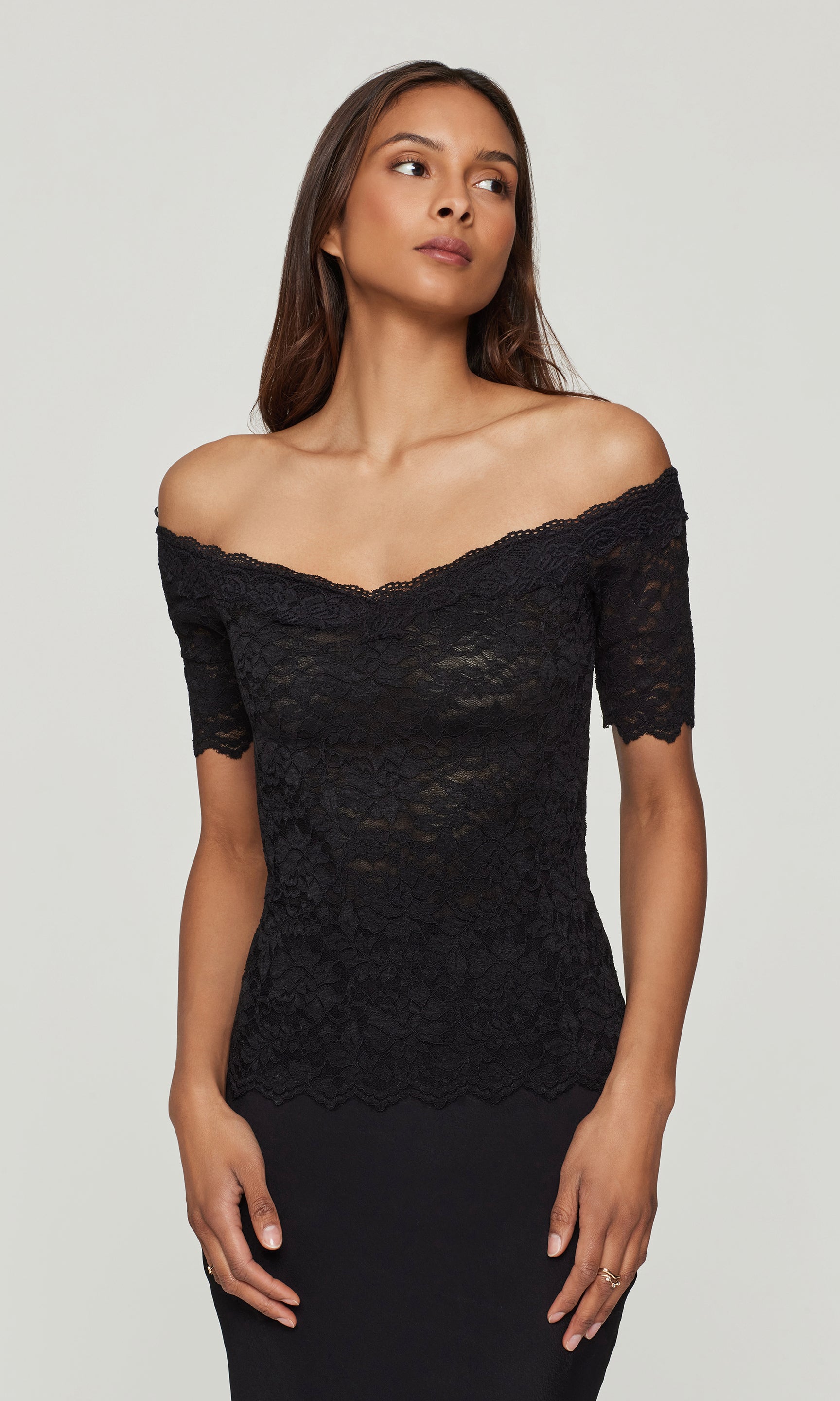Woman wearing a black lace off-shoulder top against a plain background