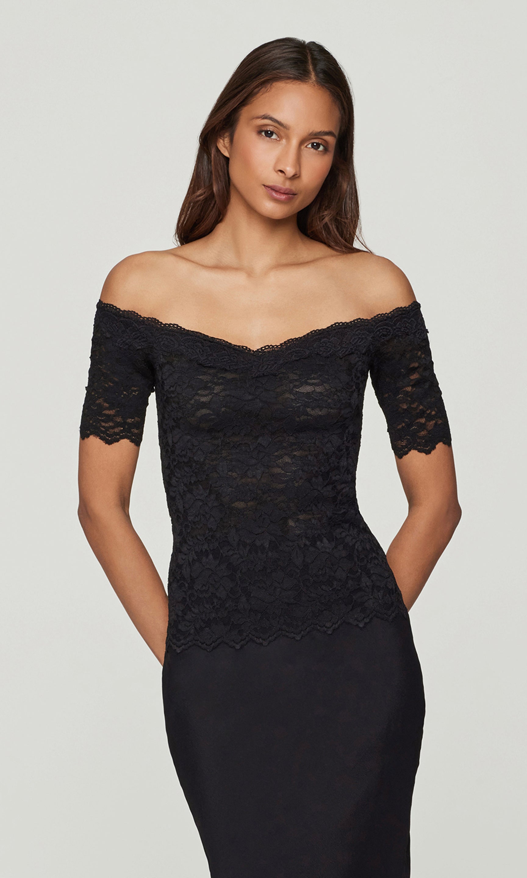 Woman wearing a black lace off-shoulder top and black skirt against a plain background