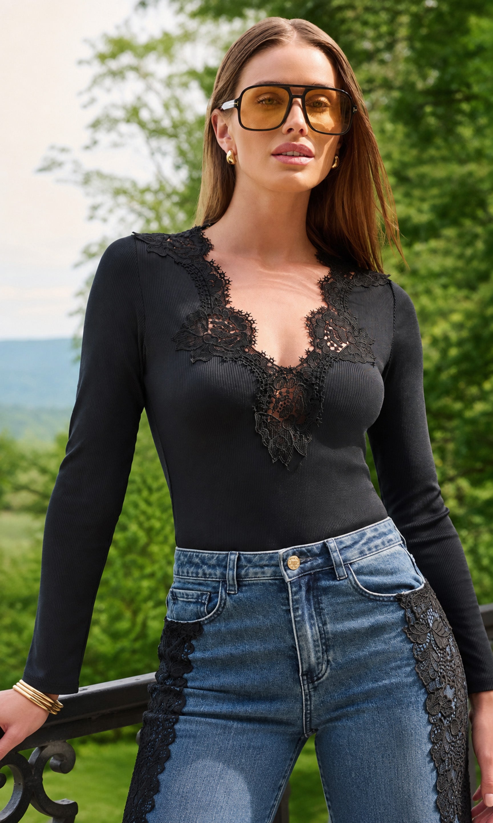 A woman wearing a black long-sleeve top with a lace V-neckline and blue jeans, standing outdoors.