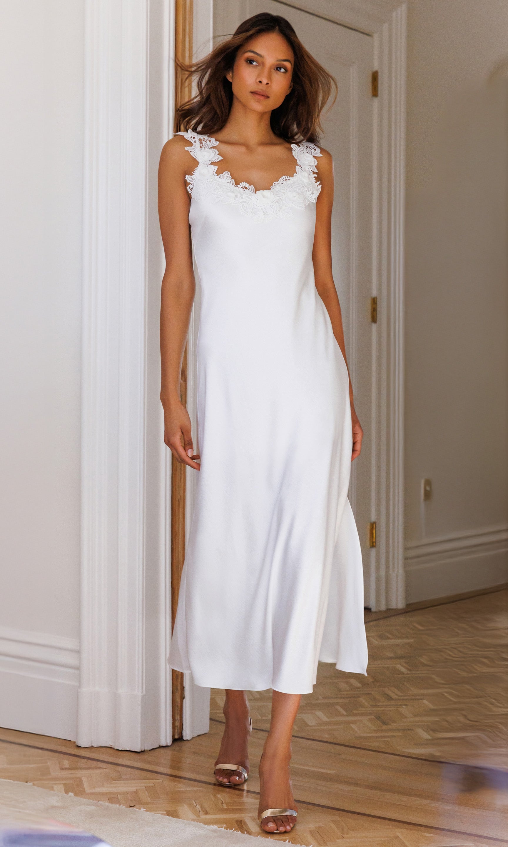 Woman wearing a white dress standing in a room with wooden flooring and white walls.