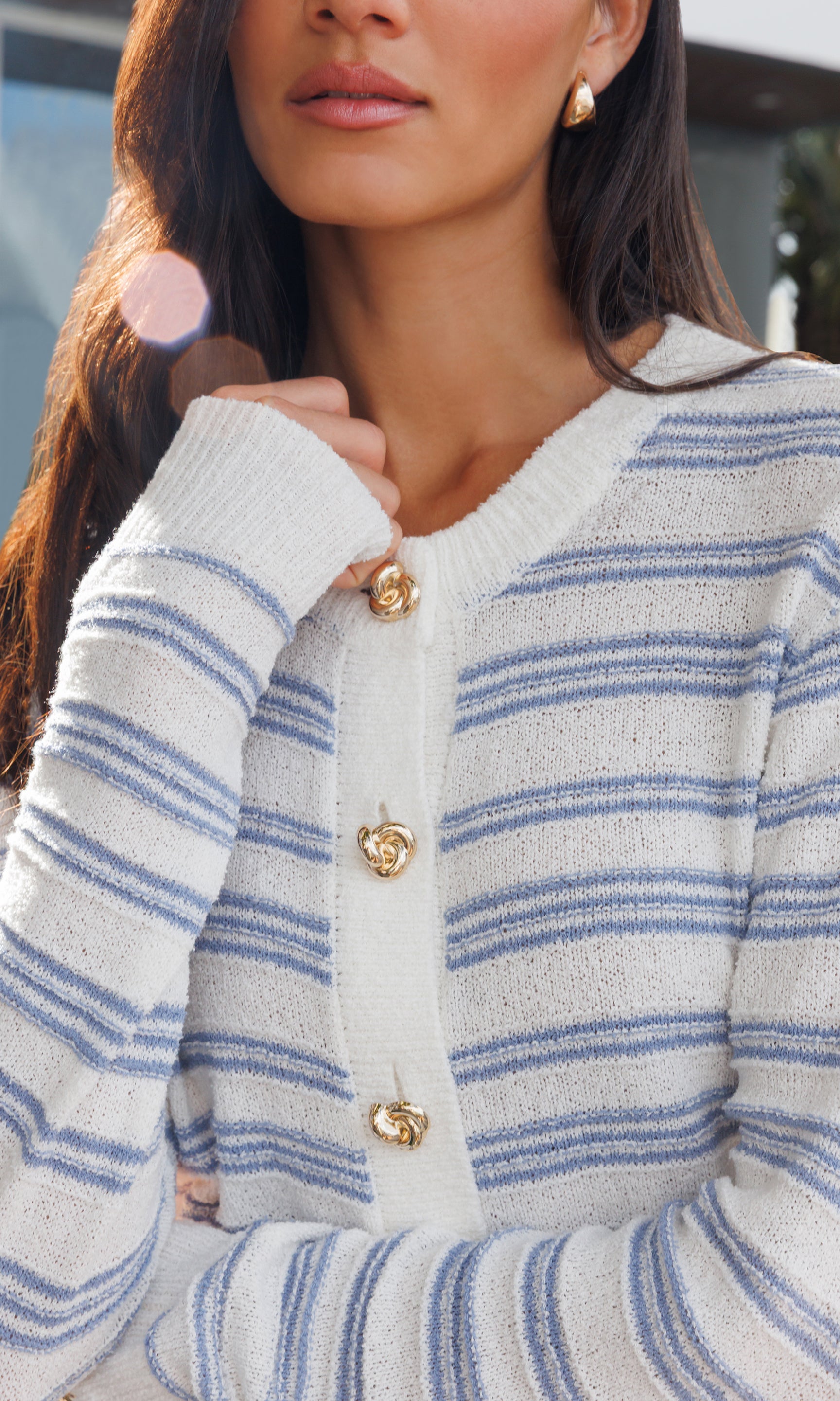 Close-up of a person wearing a blue and white striped cardigan with gold buttons.