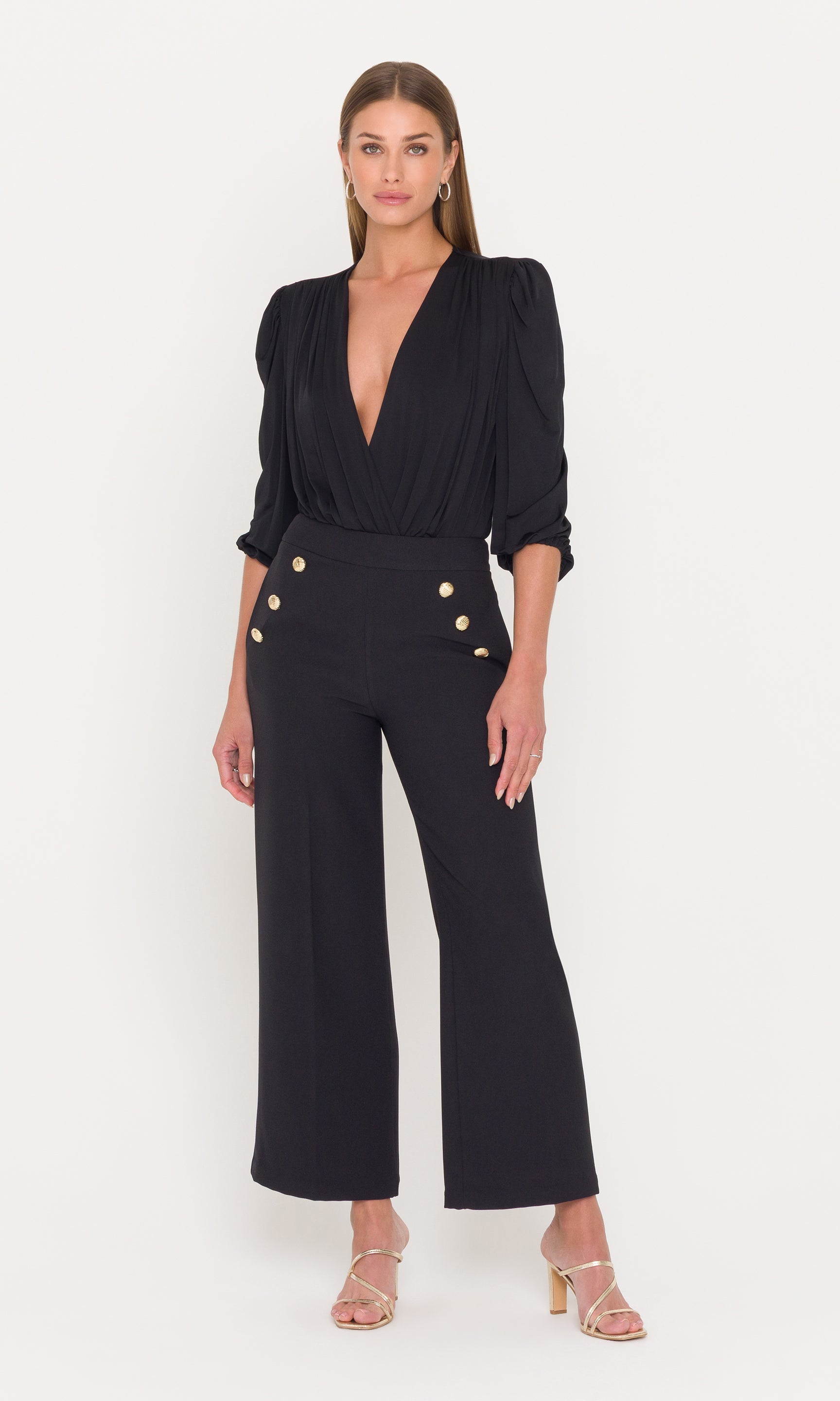 Full body image of woman wearing a black bodysuit with black pants with gold buttons on a white background