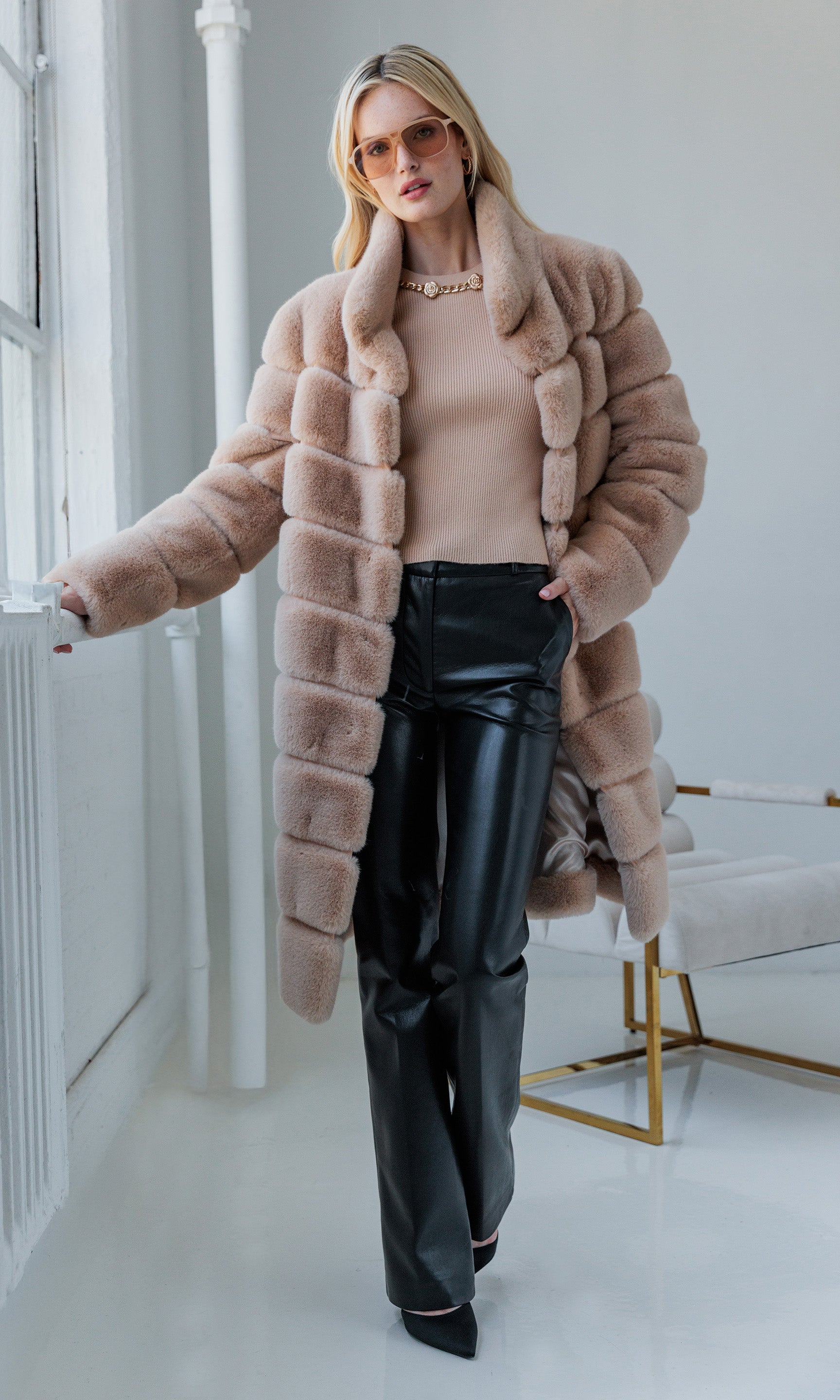 Full body view of the model in the pants and beige fur, standing in a bright room.