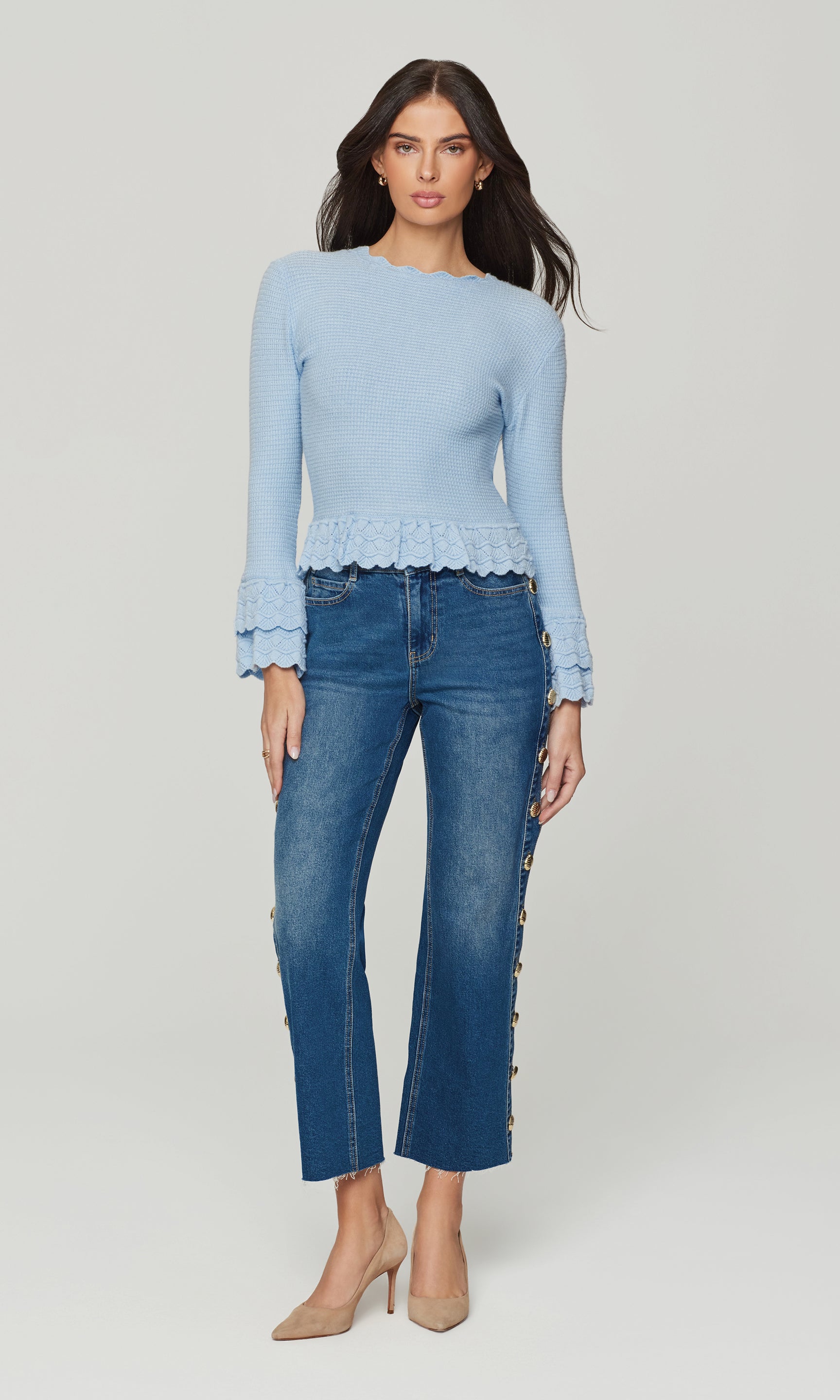 Full body view of woman wearing a light blue sweater with lace trim and blue jeans on a white background