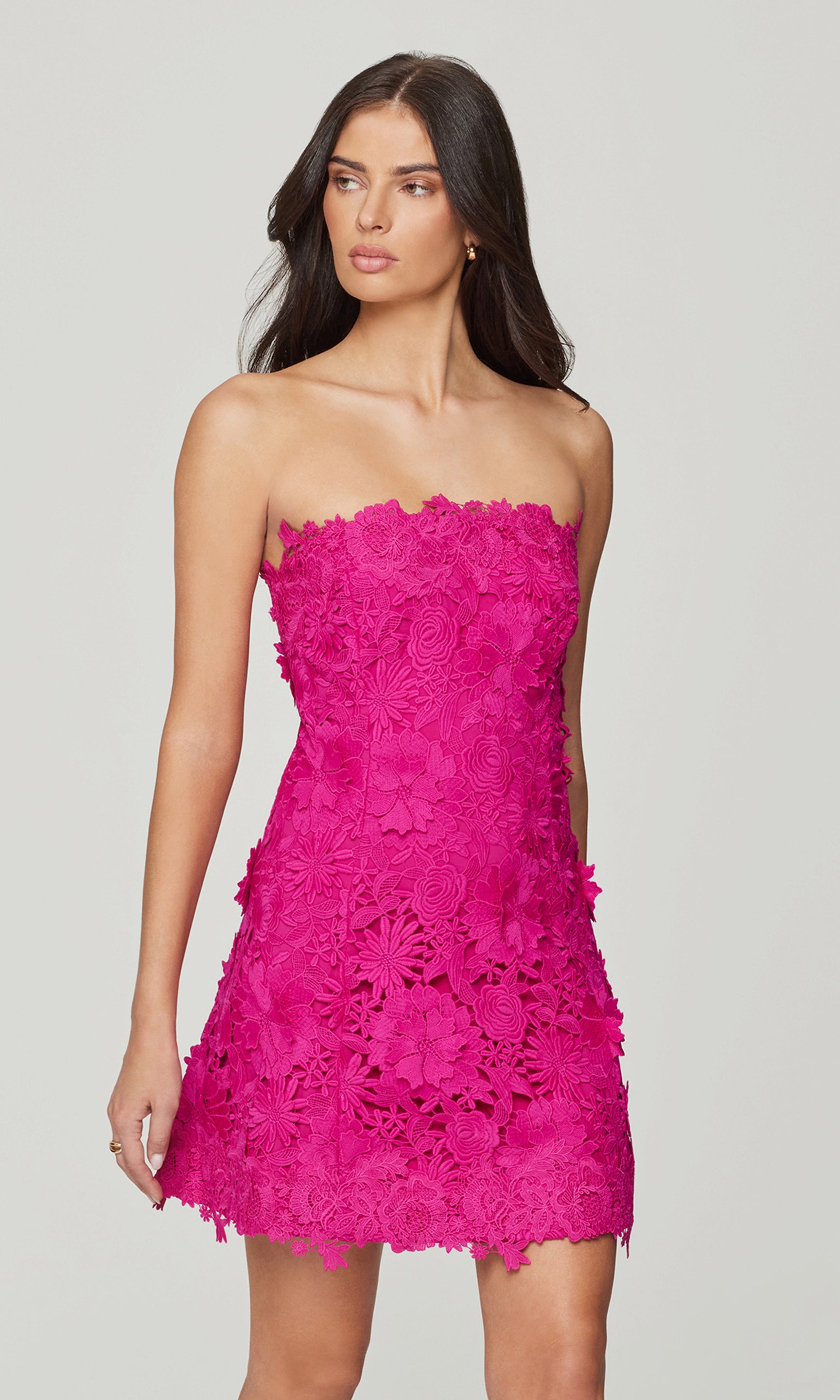 Side view of woman wearing a bright pink strapless lace dress on a light gray background