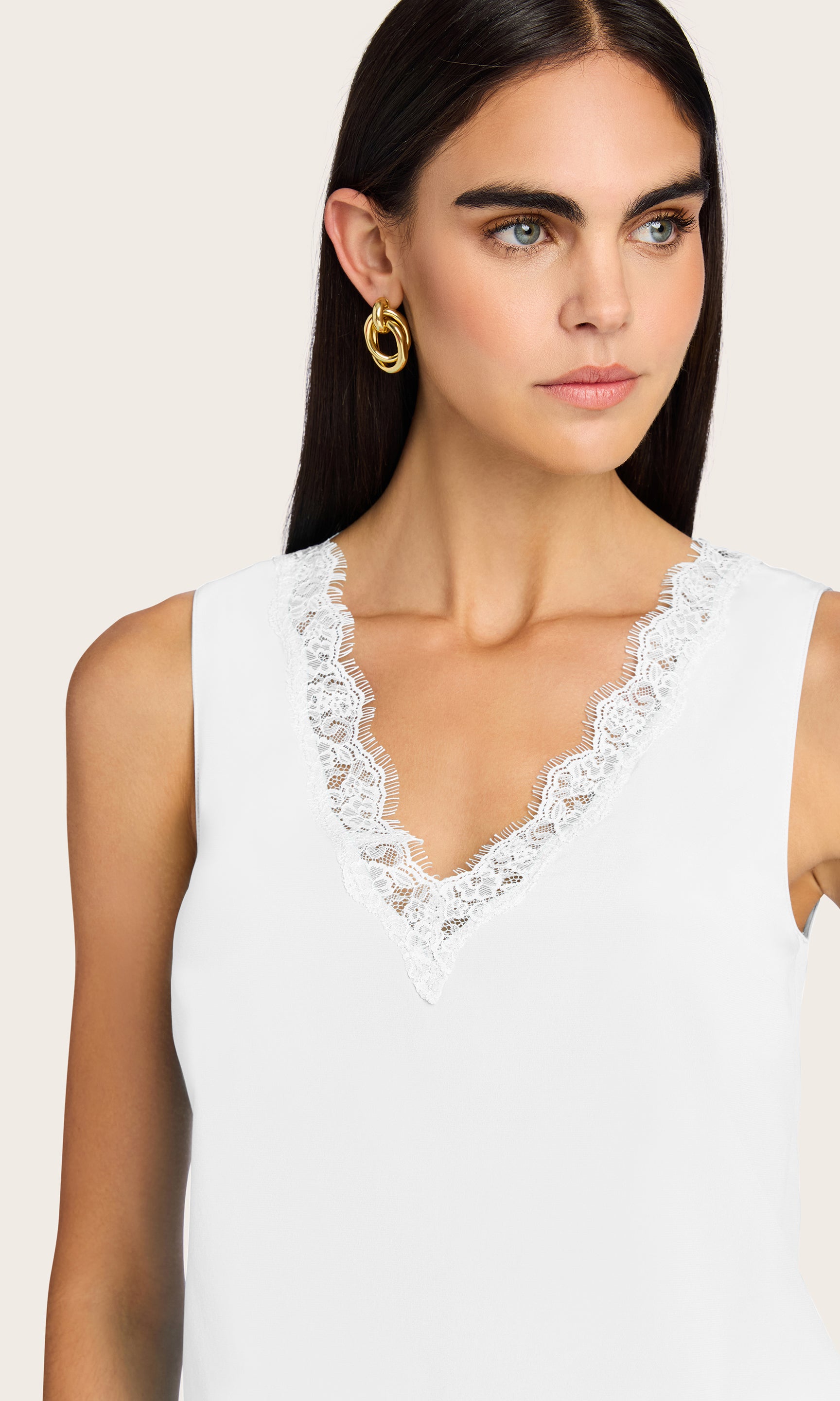 Woman wearing a white sleeveless top with lace detailing on a beige background