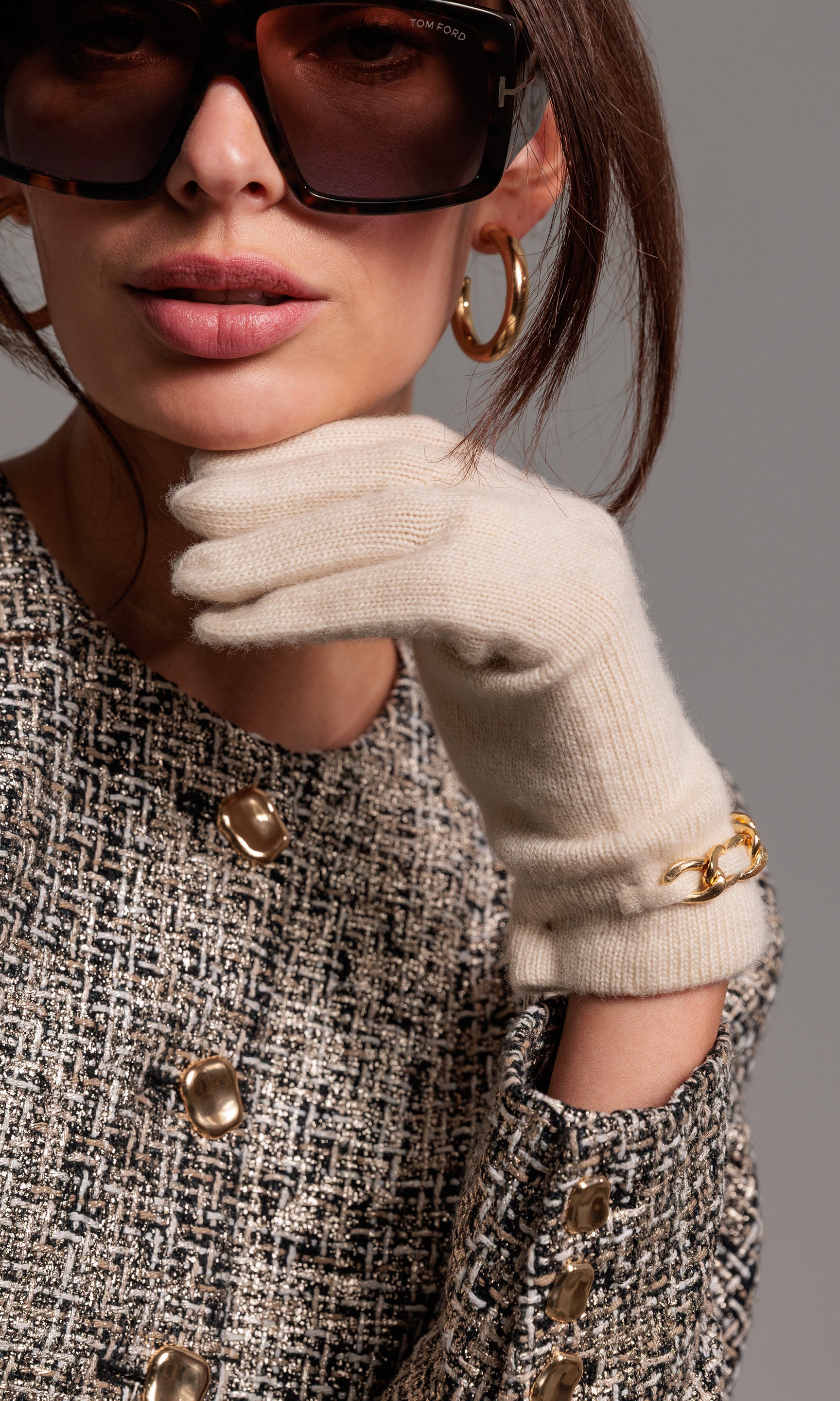 Close-up of a person wearing sunglasses, a textured coat, and a beige glove on a gray background