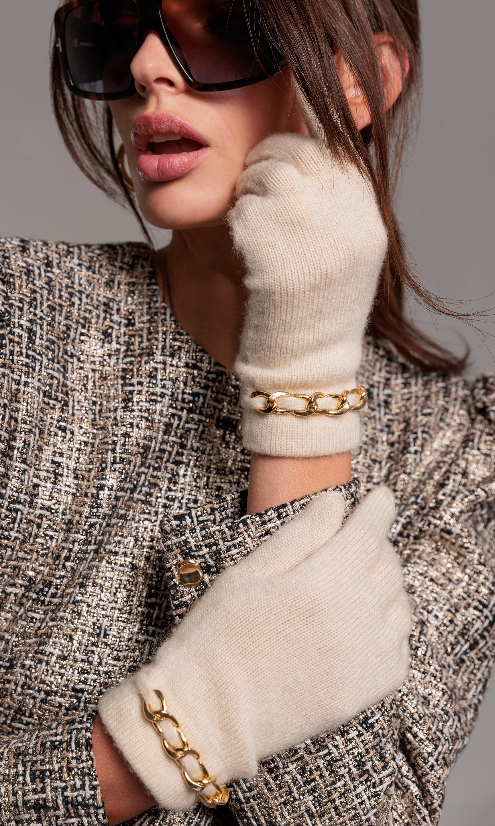 Person wearing white gloves with gold accents and a textured coat on a gray background